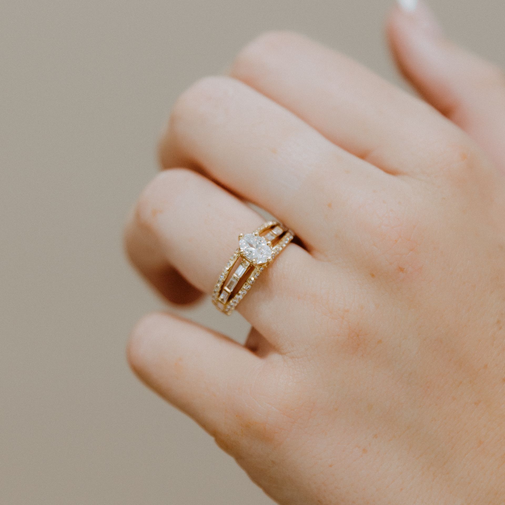 Hand wearing a gold engagement ring with a central oval stone and a split band with pave diamonds.