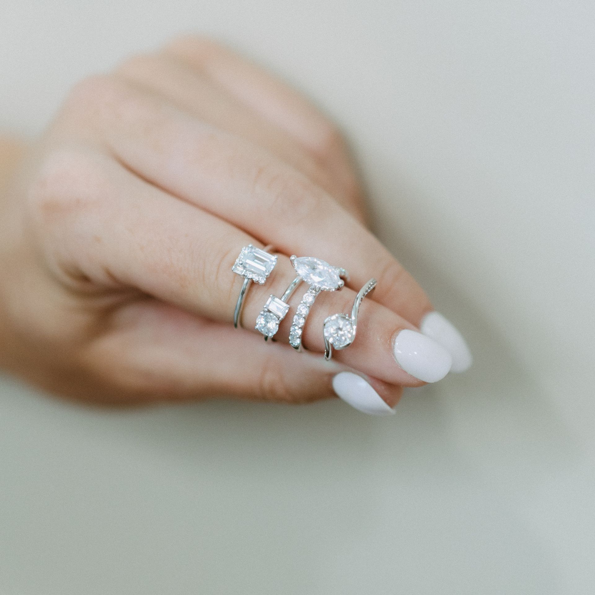 Hand holding four diamond rings, with white nails against a light background.