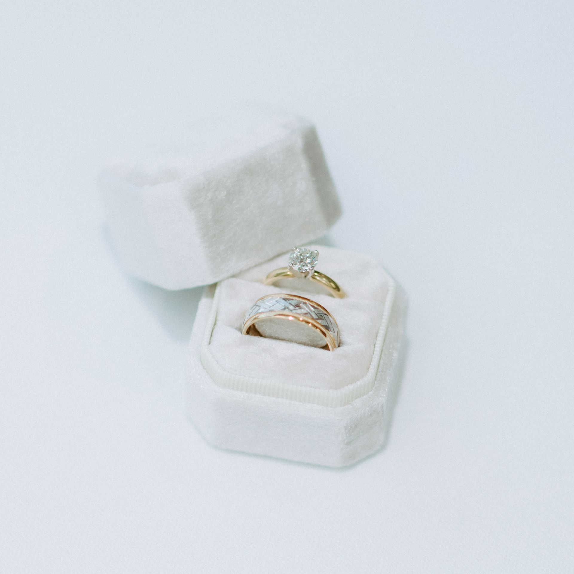 White velvet ring box with two rings inside. One gold, one with a diamond.