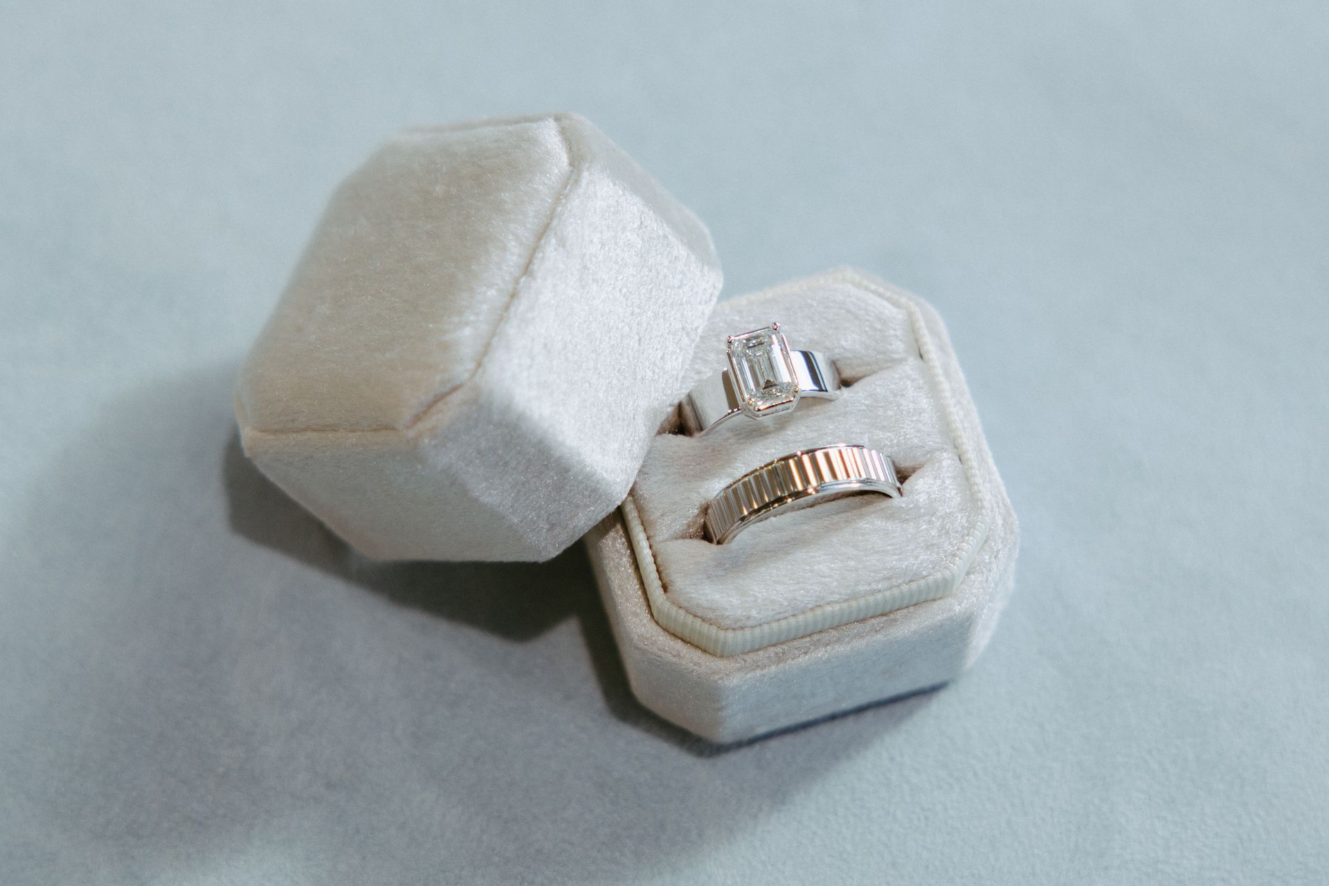Two rings in a white velvet octagonal ring box, open. One ring has a large emerald-cut diamond.