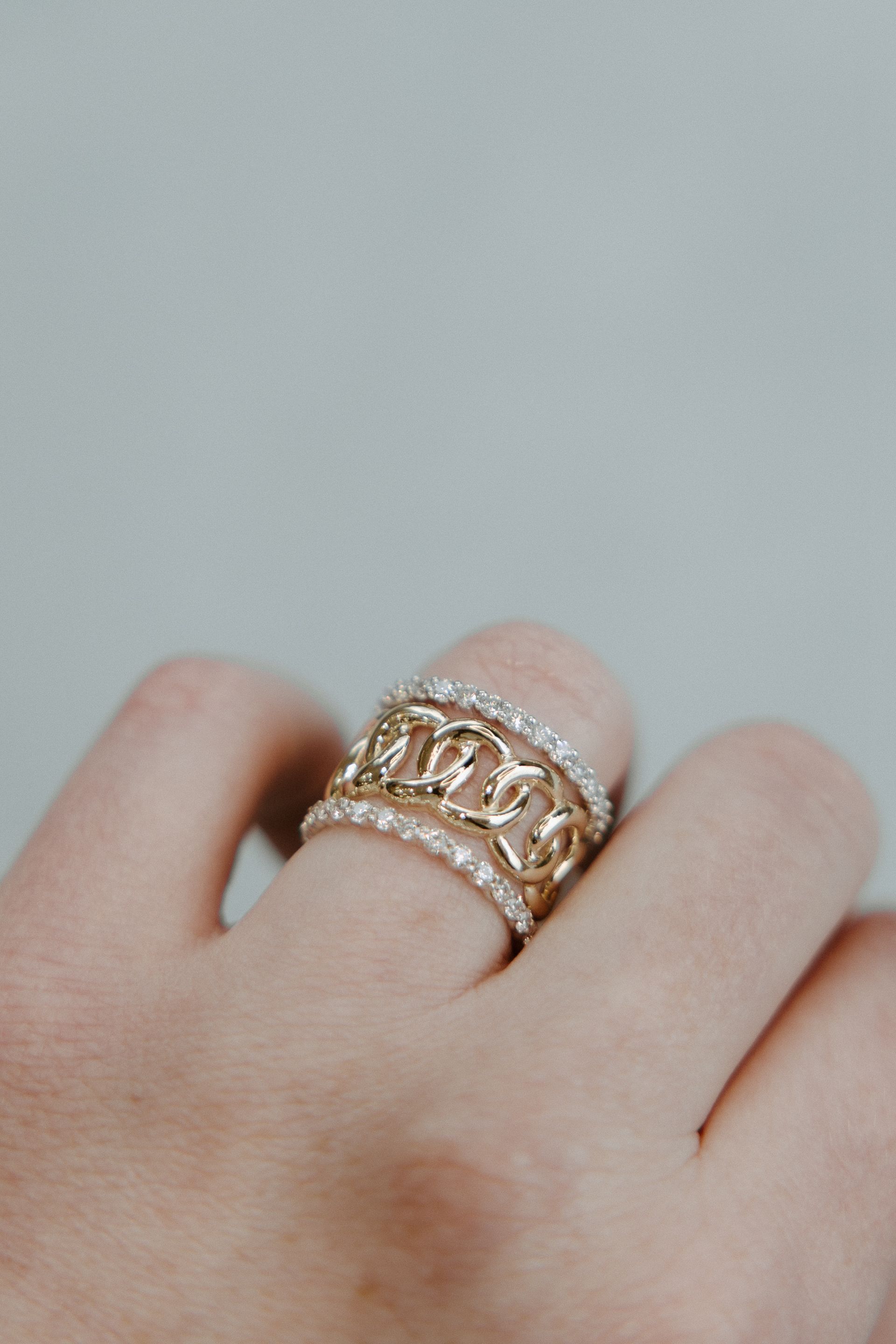 Hand wearing three gold rings, one with a chain design, the others with small gems.