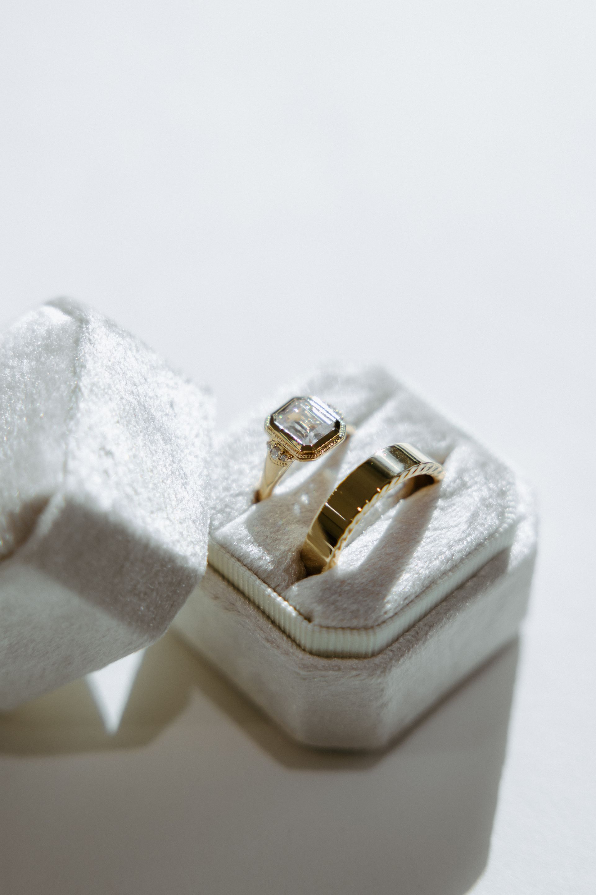 Two gold wedding rings in a white velvet ring box, lit with soft light.