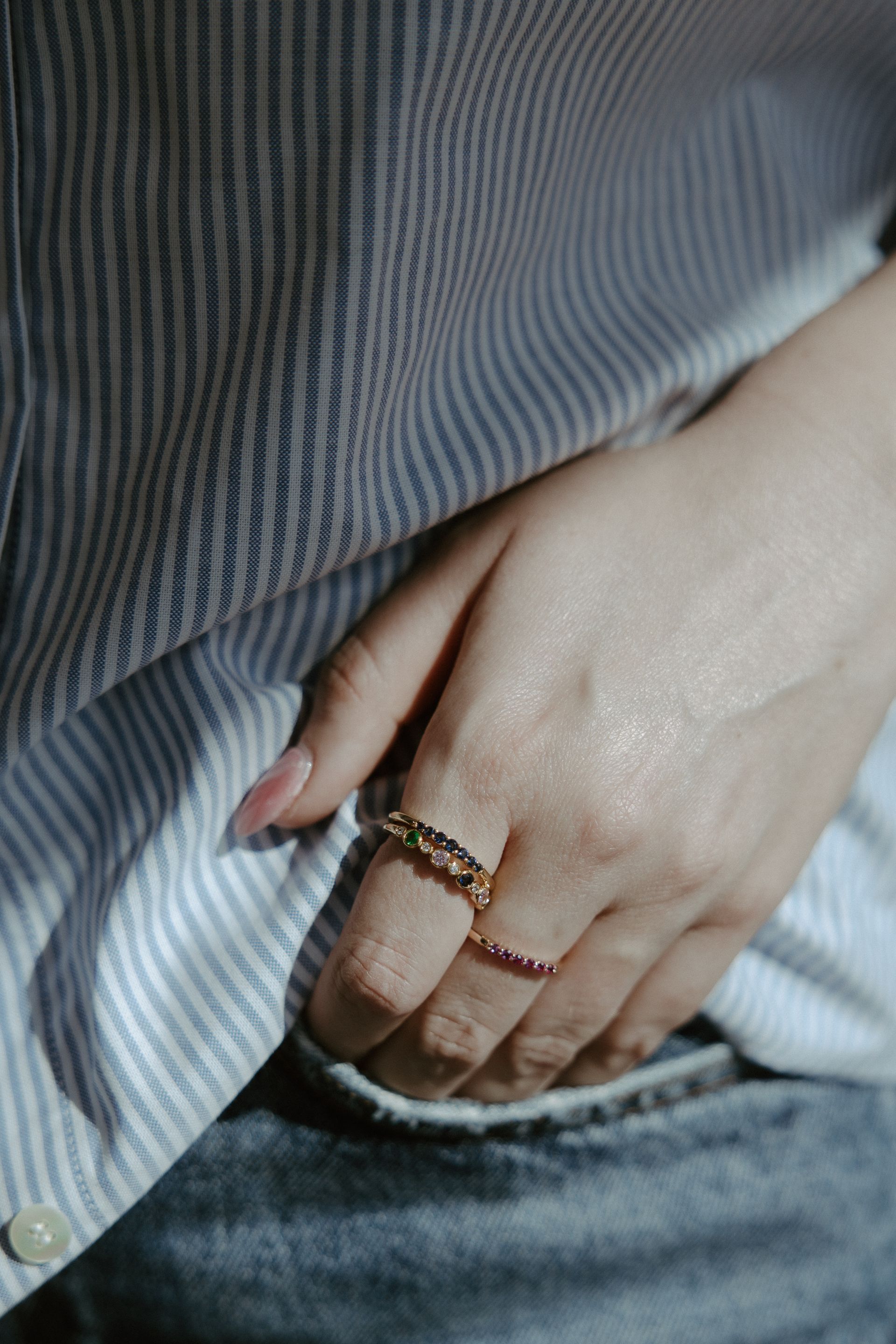 Hand wearing two gold rings on a striped shirt and jeans.