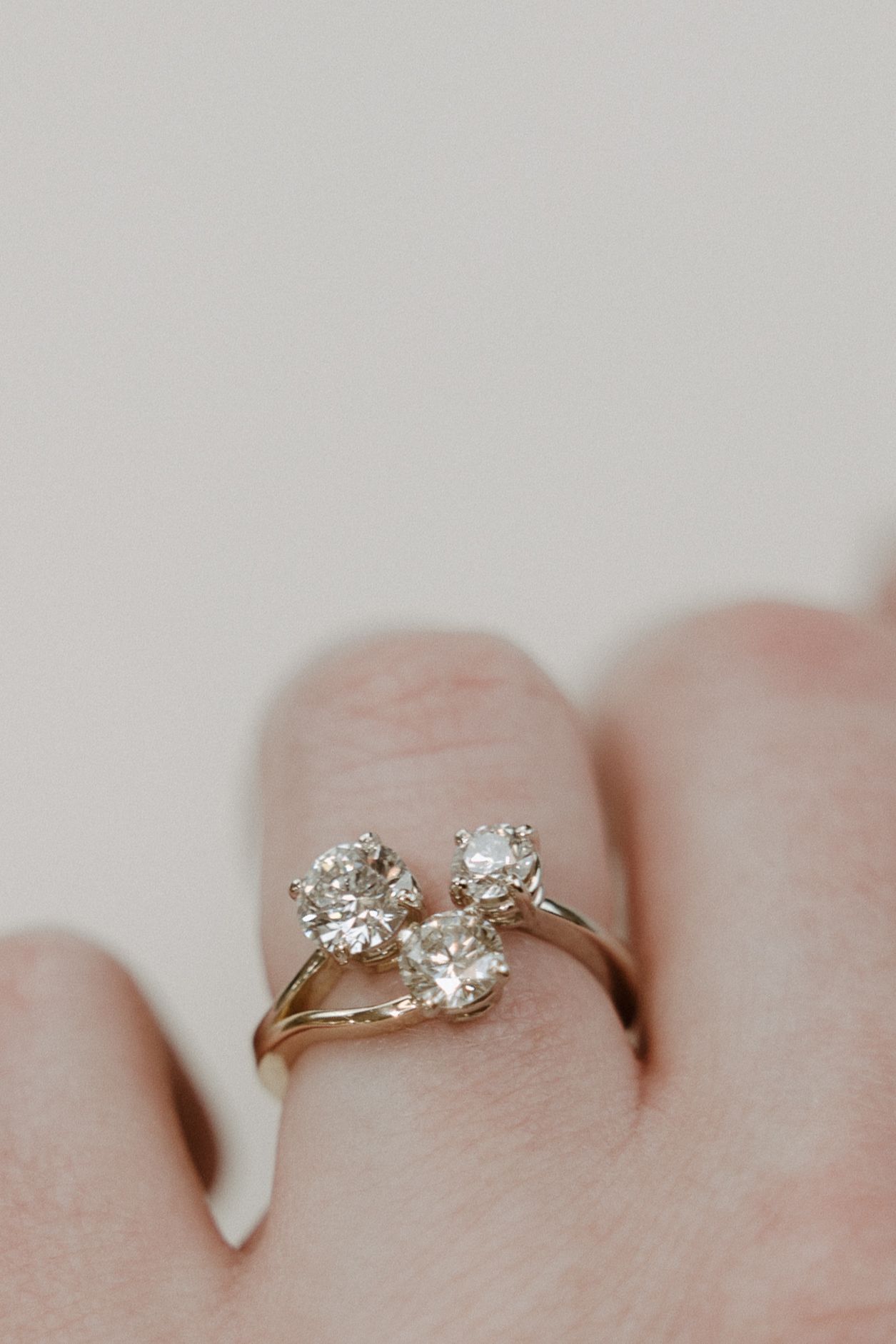 Diamond engagement ring on a finger, featuring three round stones on a gold band.