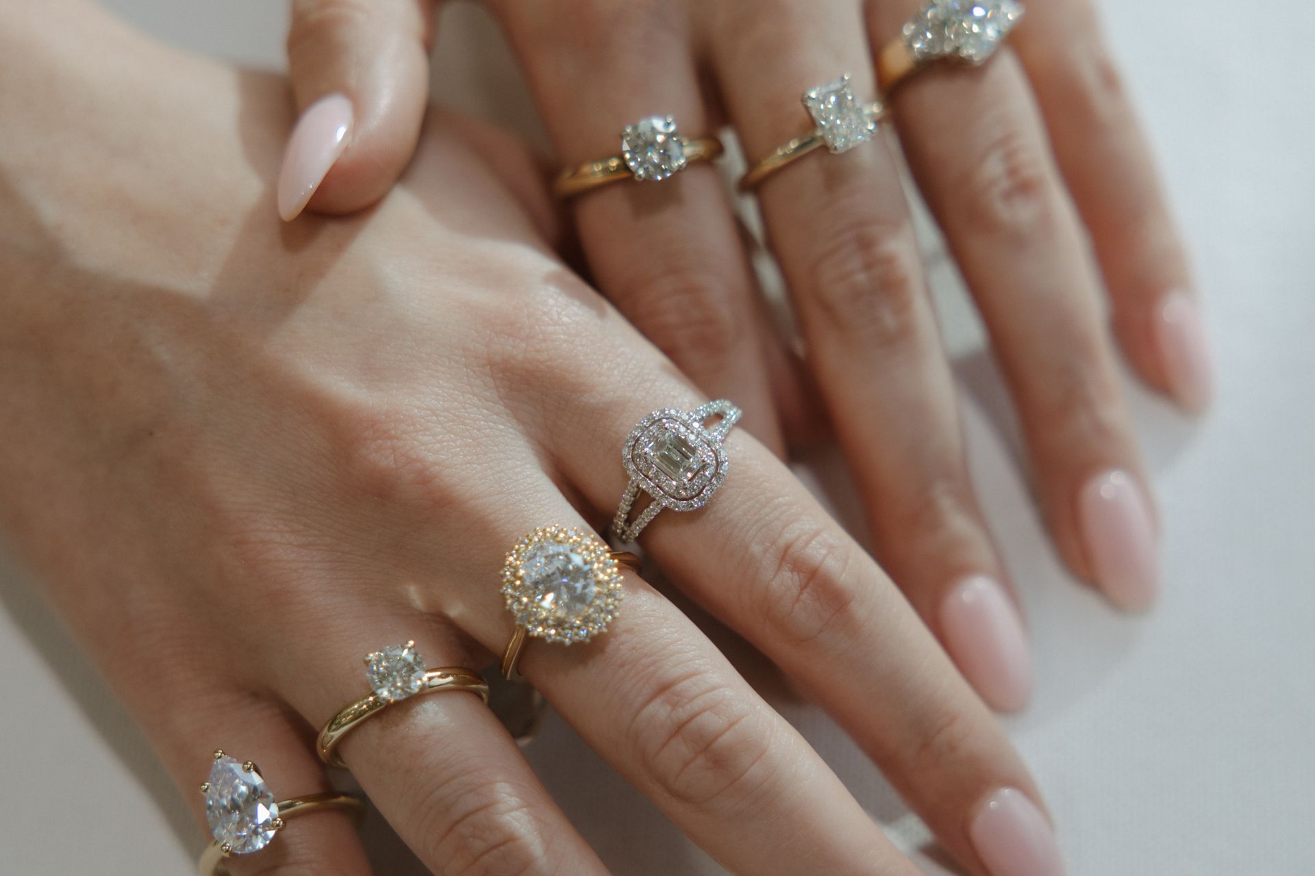 Hands displaying several diamond engagement rings.