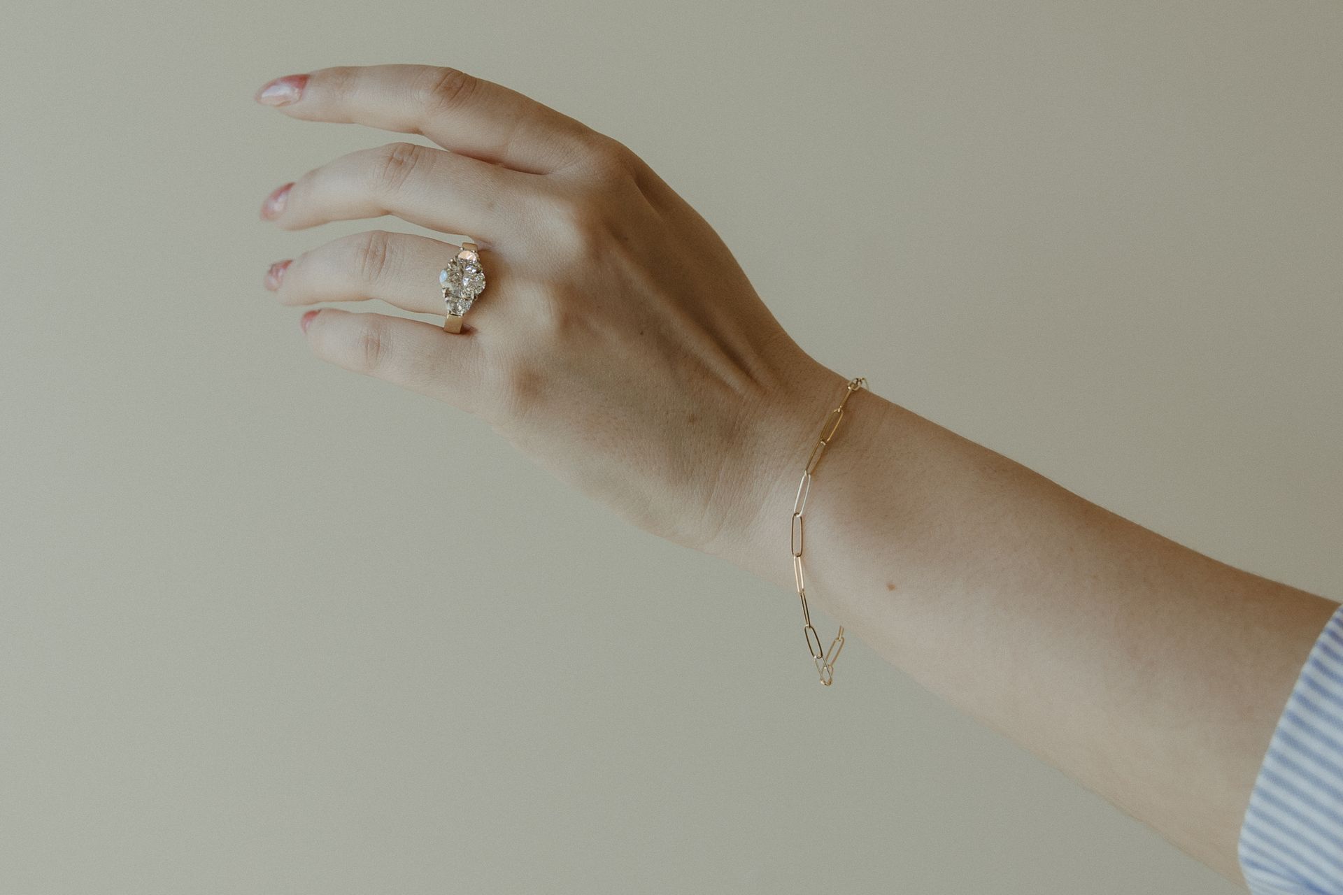 Hand wearing a ring and bracelet, against a light background.