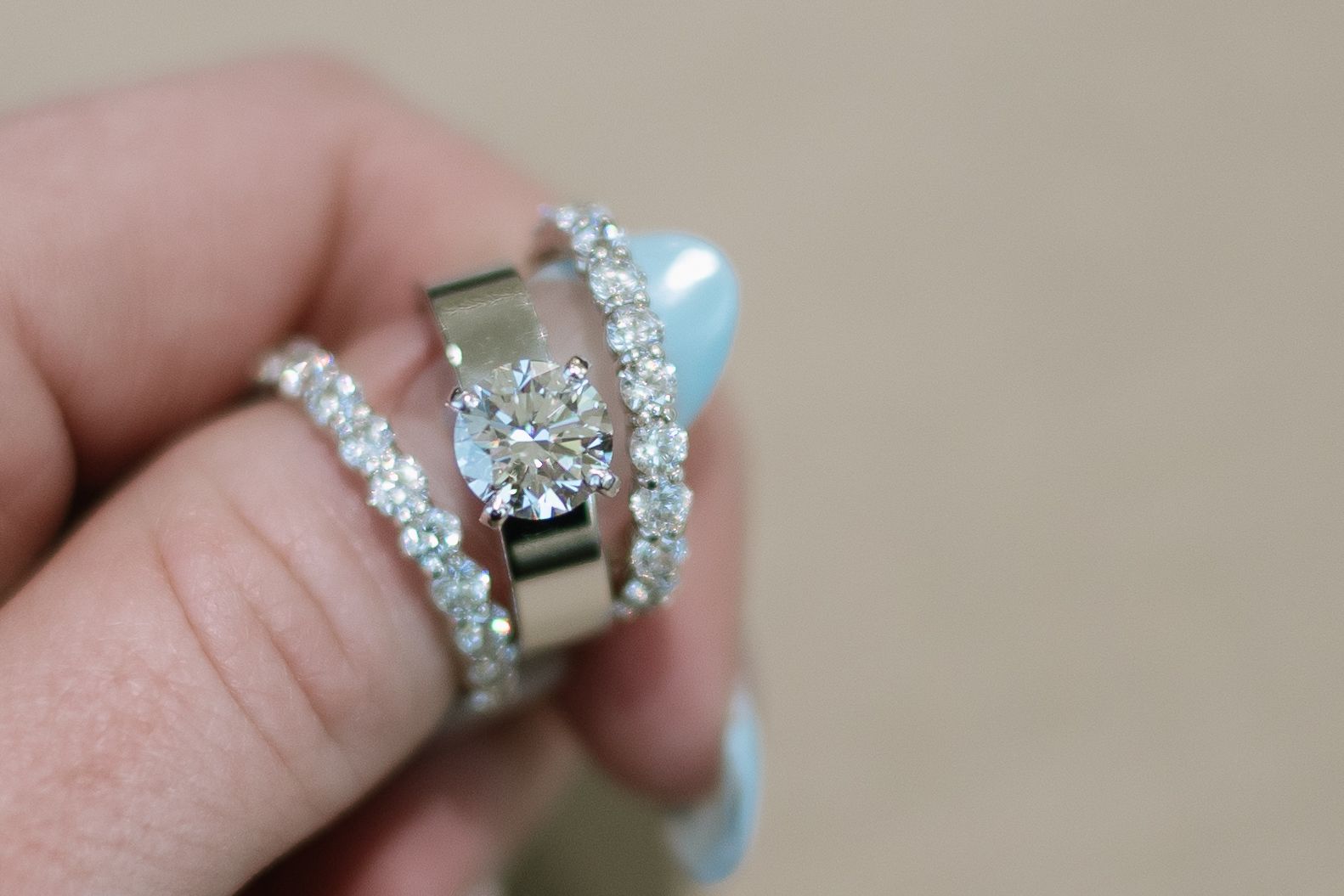 Hand holding three diamond rings. One is solitaire, two have small diamonds.