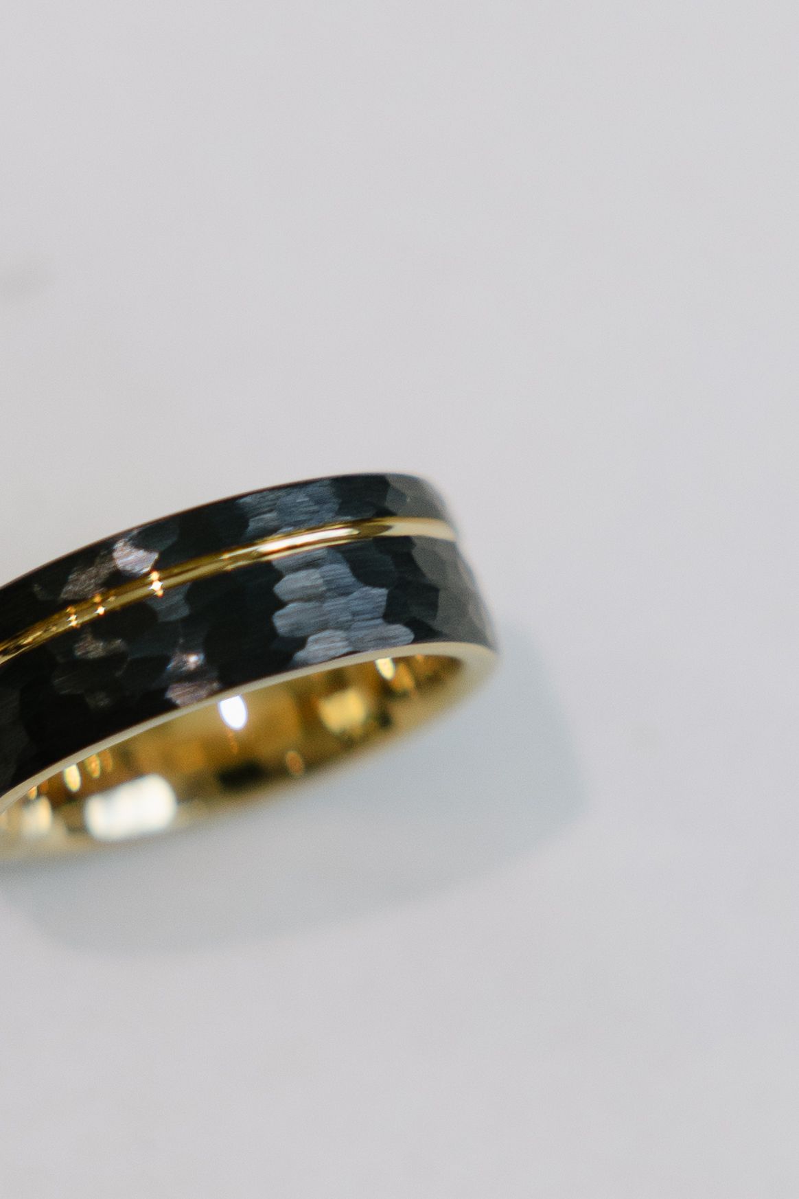 Black and gold ring with hammered texture and a gold stripe, resting on a white surface.