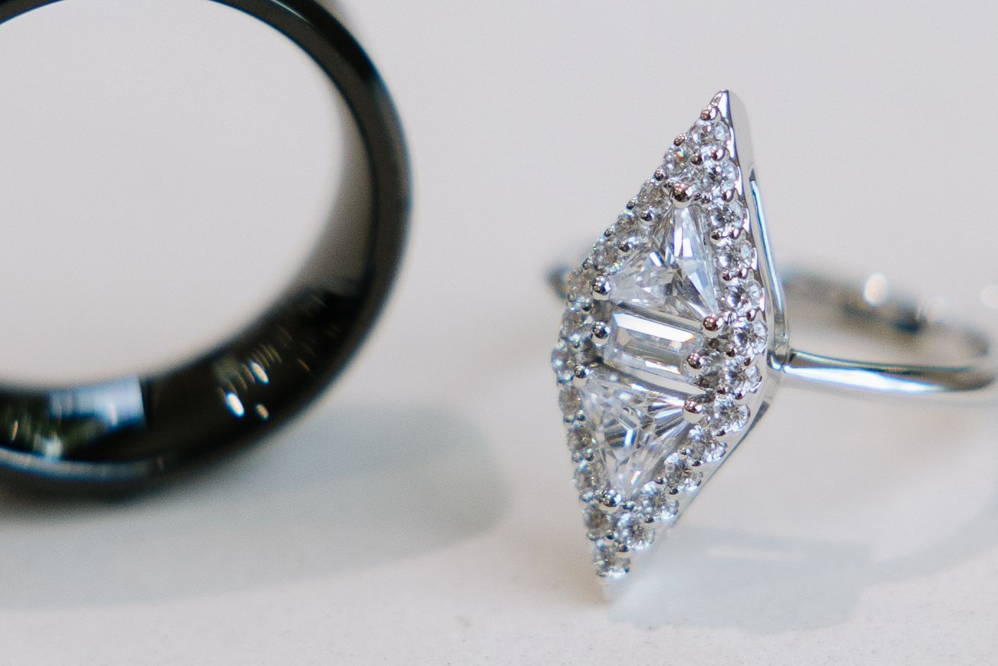 Diamond engagement ring with a baguette and round diamond cluster, next to a black wedding band.