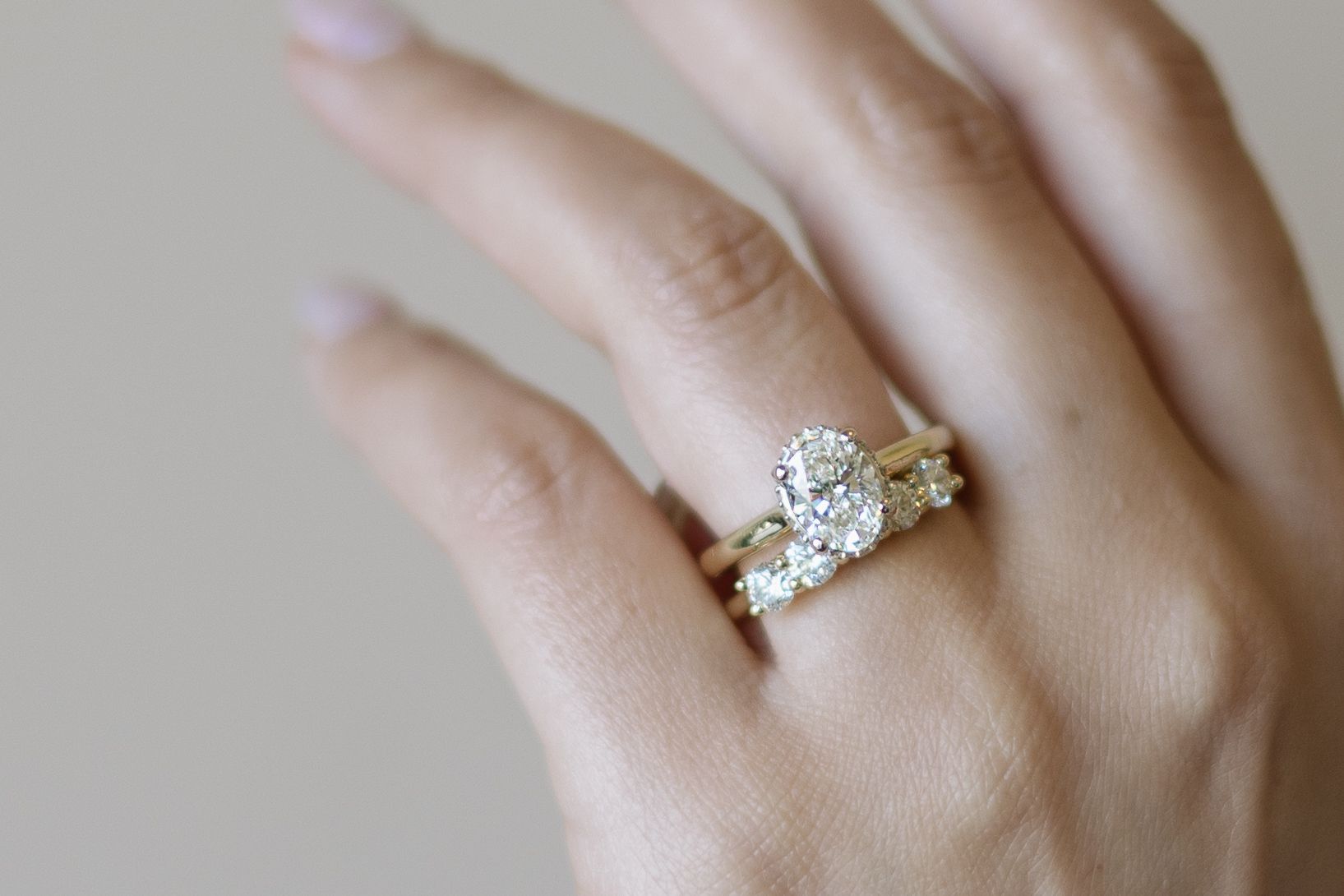 Close-up of a hand wearing a gold engagement ring with an oval diamond and a matching floral-shaped band.