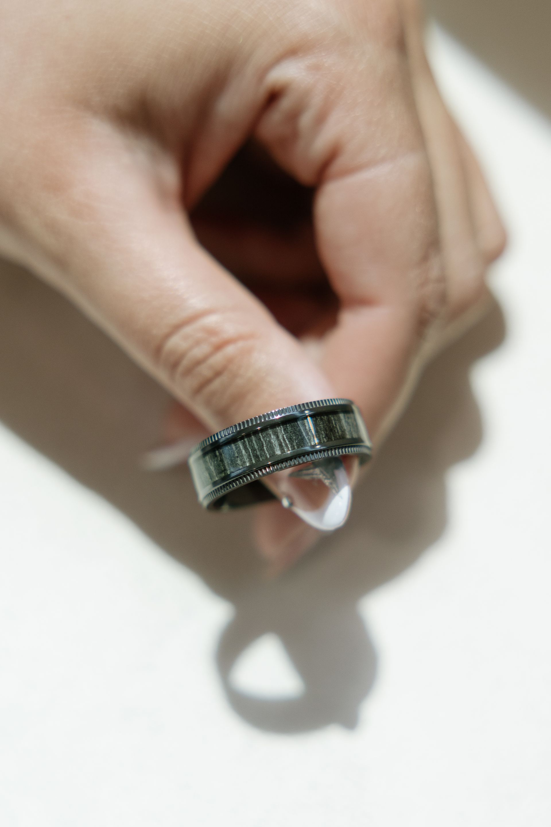 Hand holding a black ring with rows of rectangular stones, on a white surface.