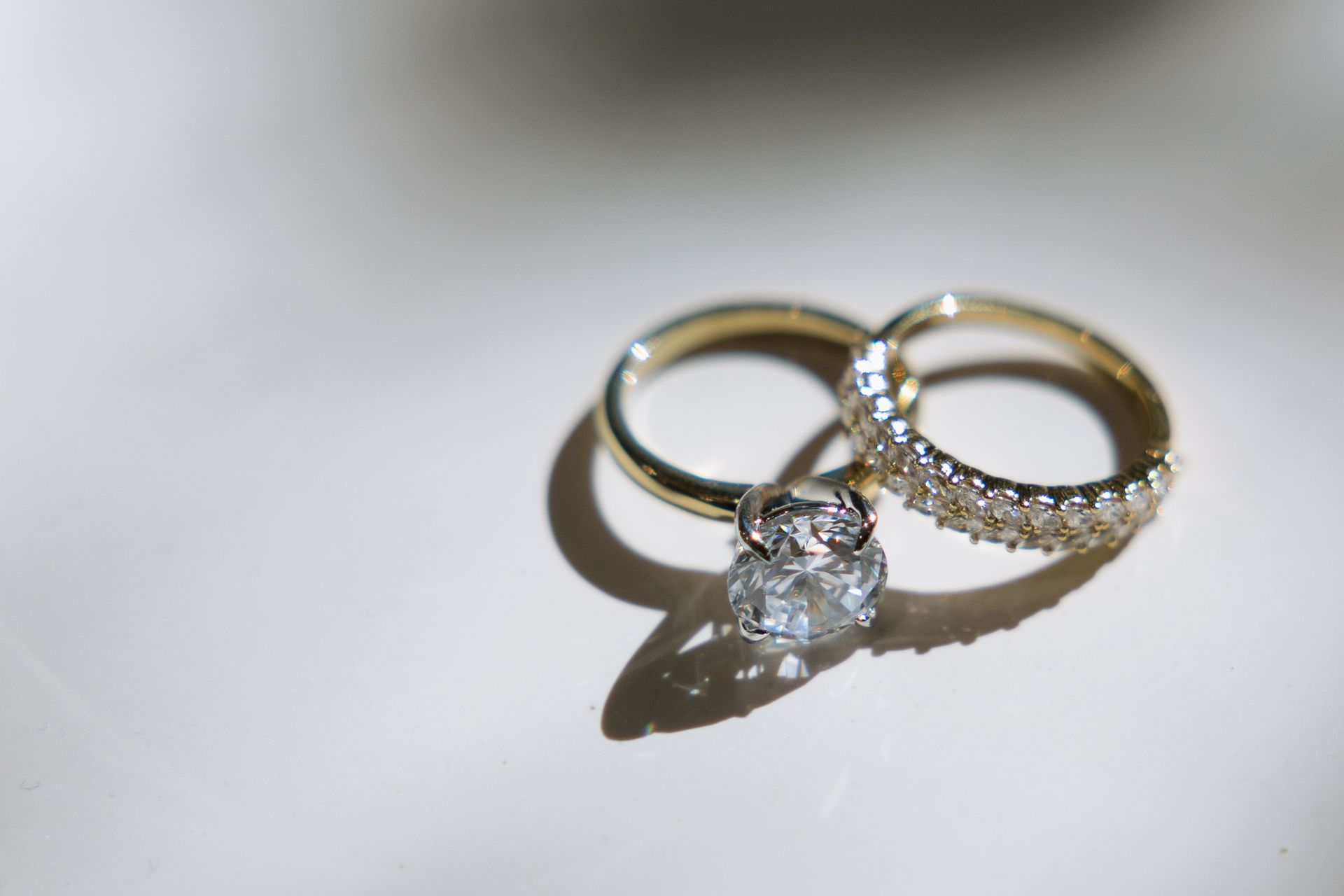 Three gold wedding rings, one with a large diamond and two bands with diamonds, on a white surface.