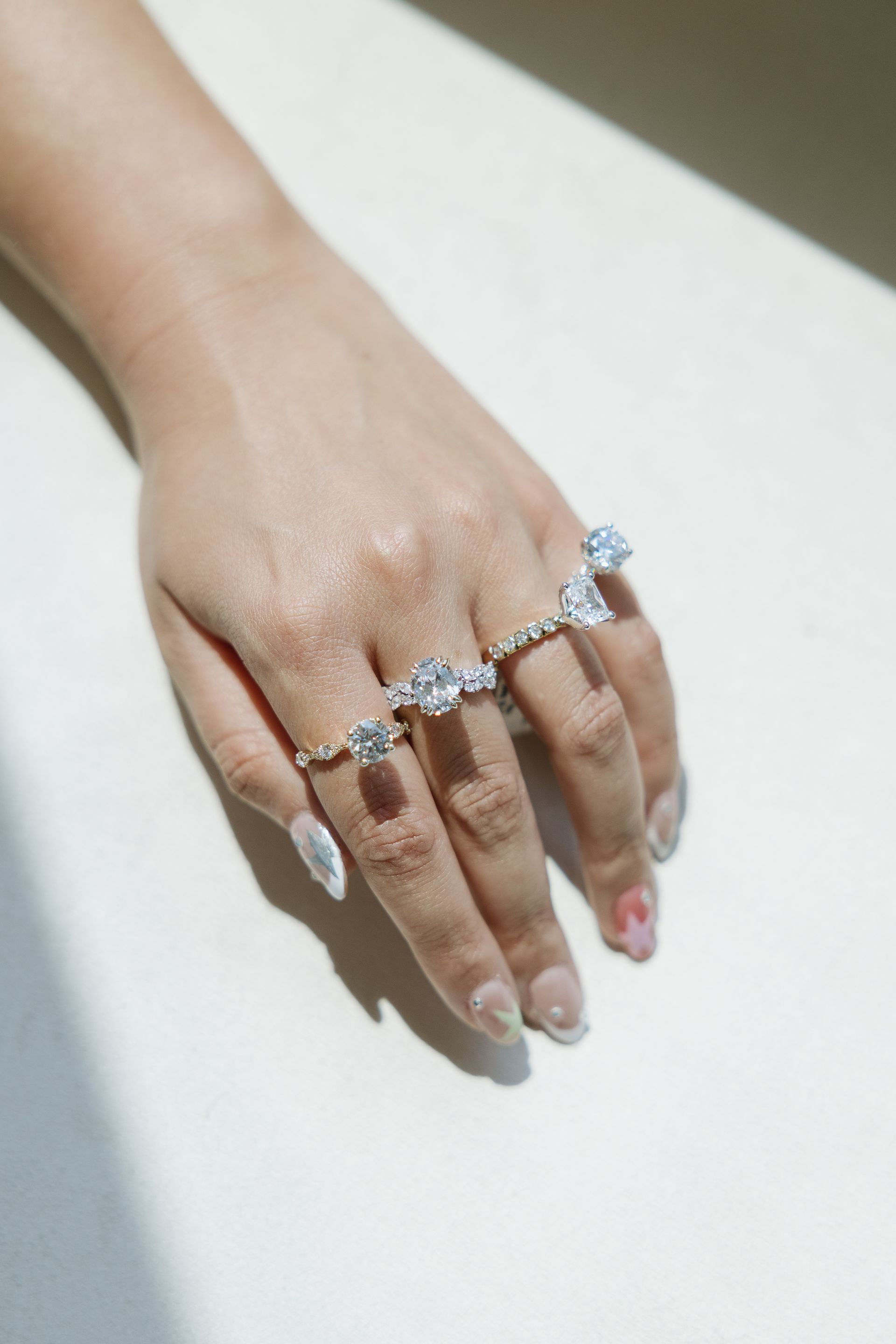 Hand with four diamond rings on a white surface, natural light.