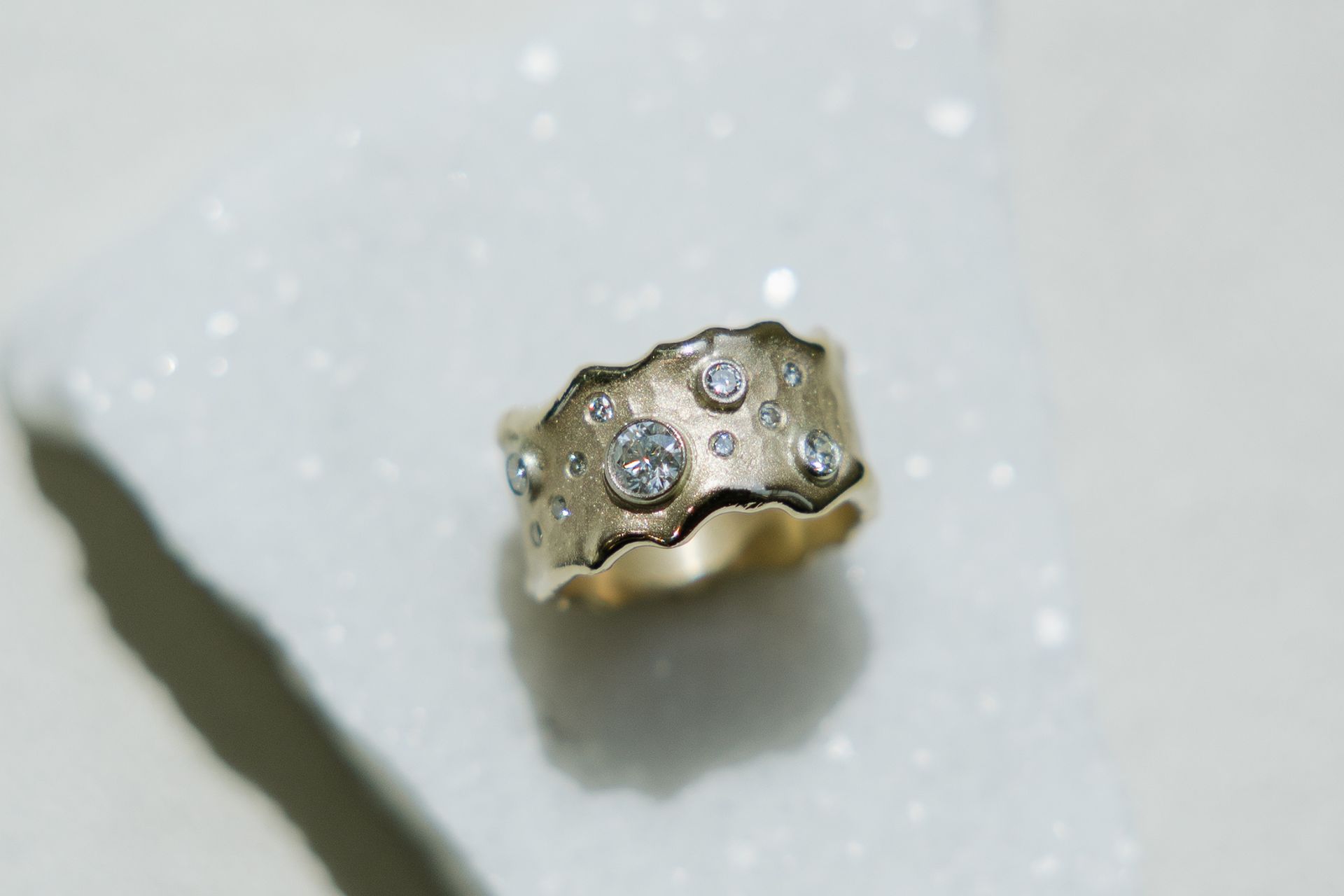 Gold ring with scattered diamonds, resting on a white, textured surface.