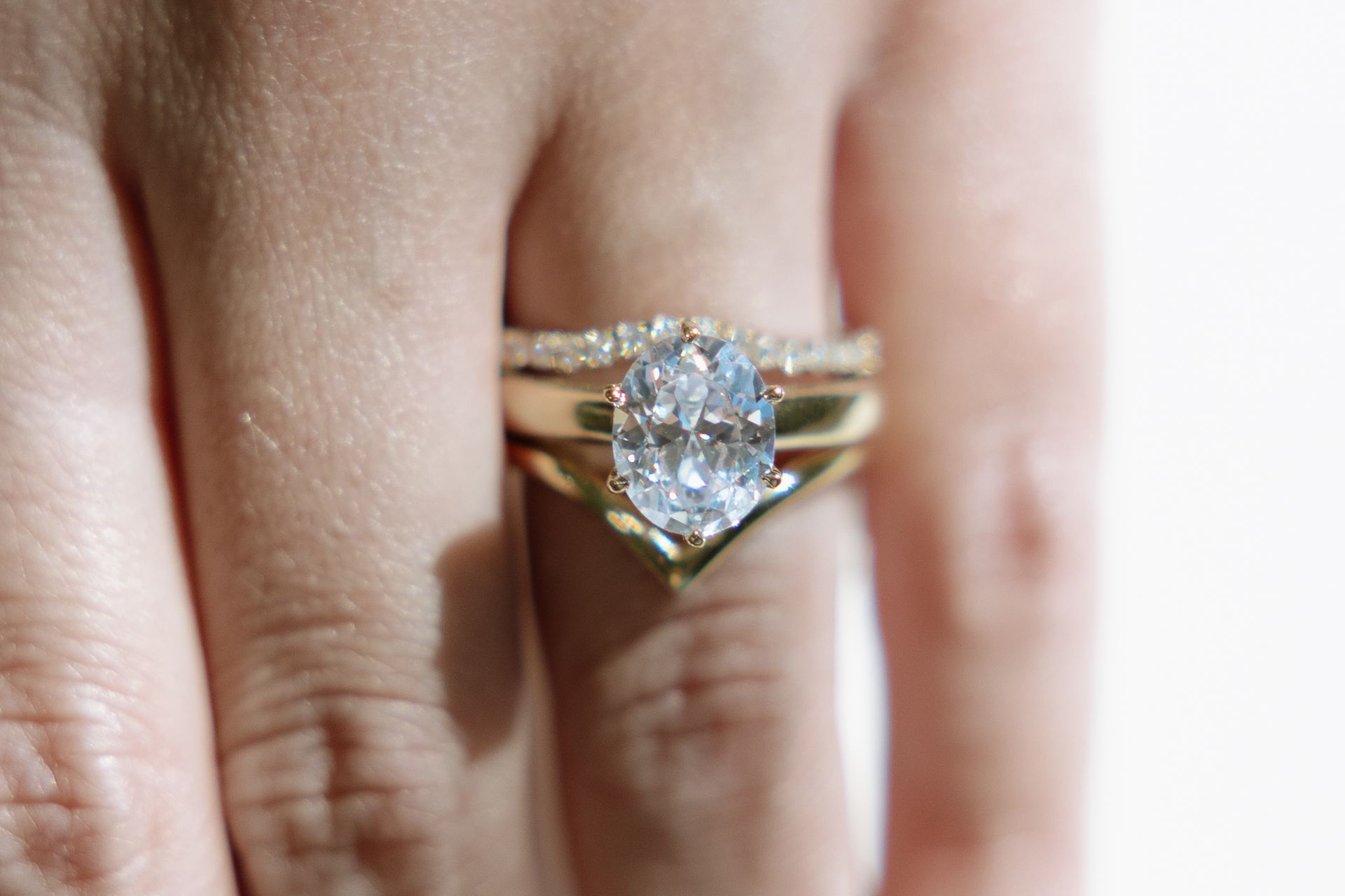 Close-up of a hand wearing three gold rings: an oval diamond ring and two curved bands.