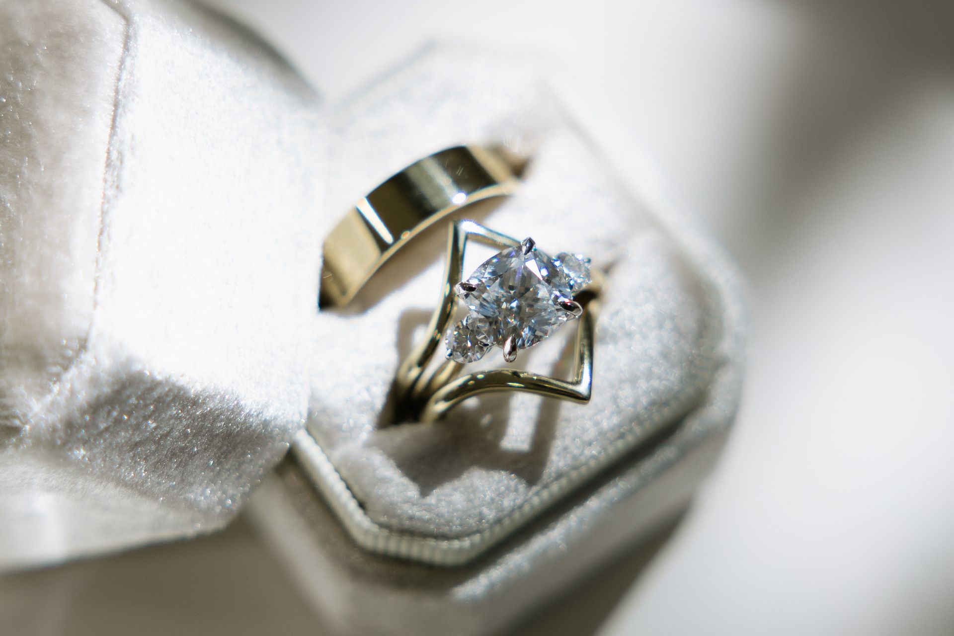 Wedding rings, gold bands, one with a diamond, in a plush, light gray ring box.