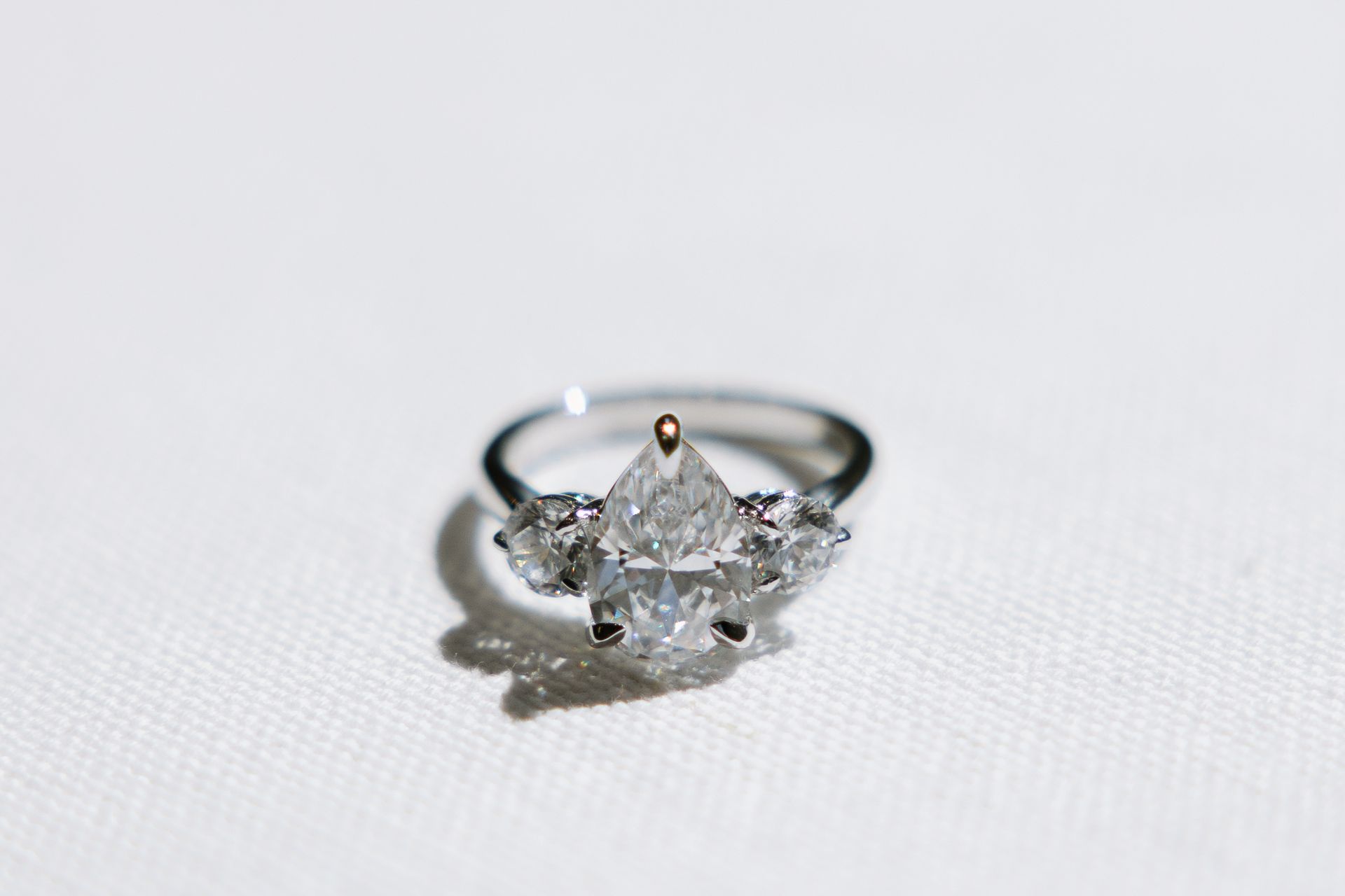 Diamond engagement ring with a pear-shaped center stone and side stones, set on a white surface.