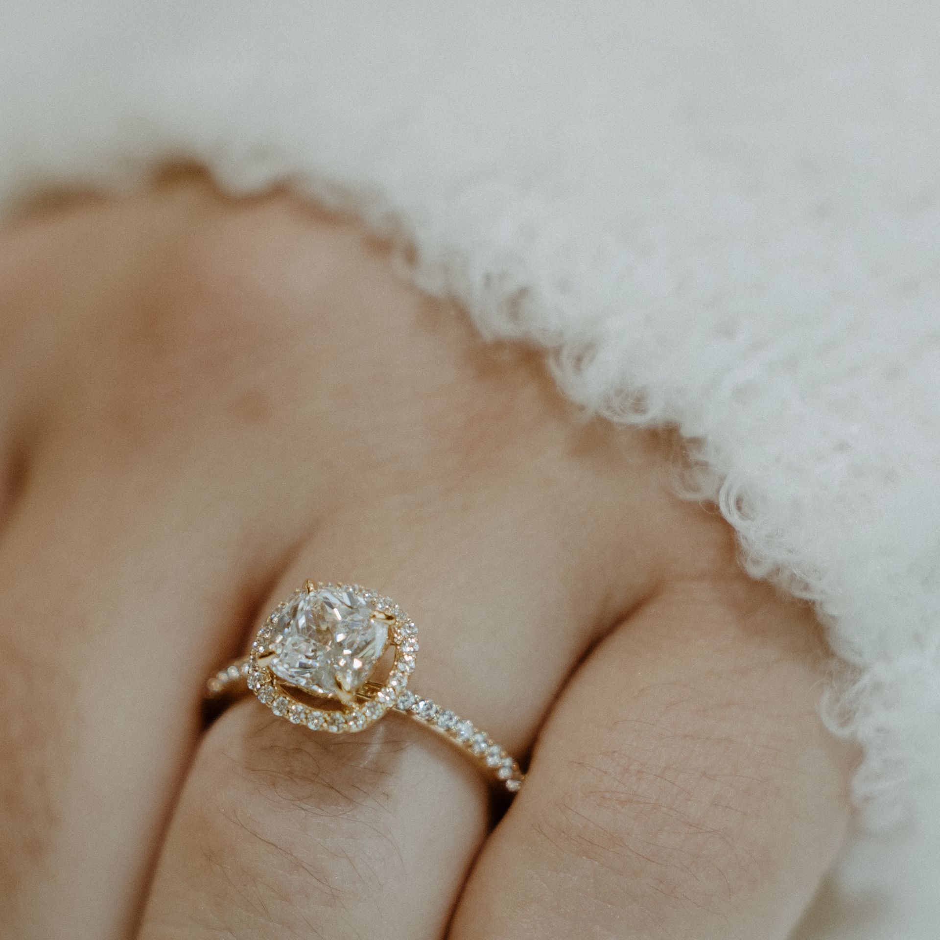 Close-up of a hand wearing a gold engagement ring with a halo of small diamonds surrounding a larger center stone.