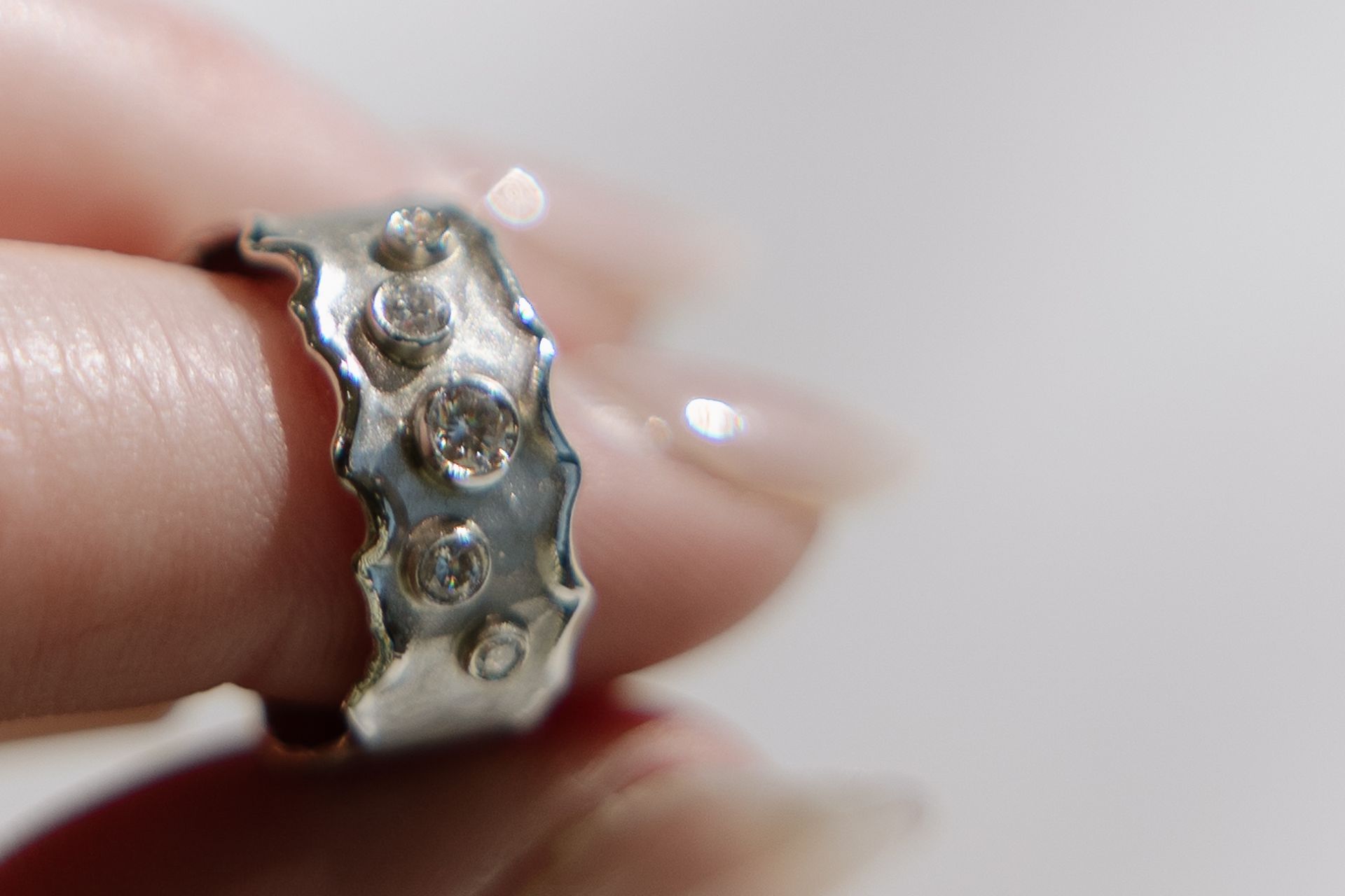 Silver ring with wavy edges and three clear stones, held by a person's fingers.