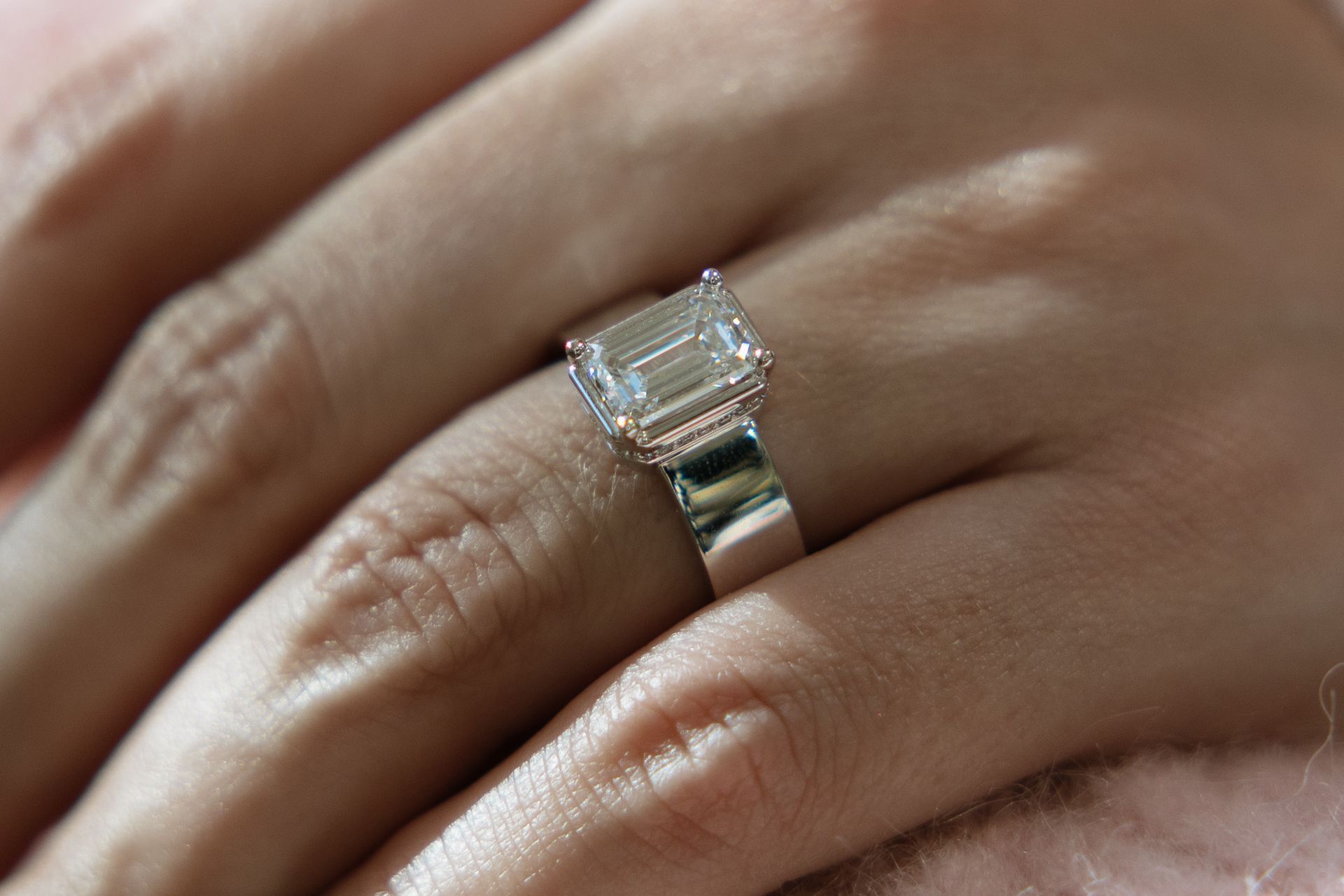 Close-up of a hand wearing a diamond ring with an emerald cut center stone, set on a silver band.