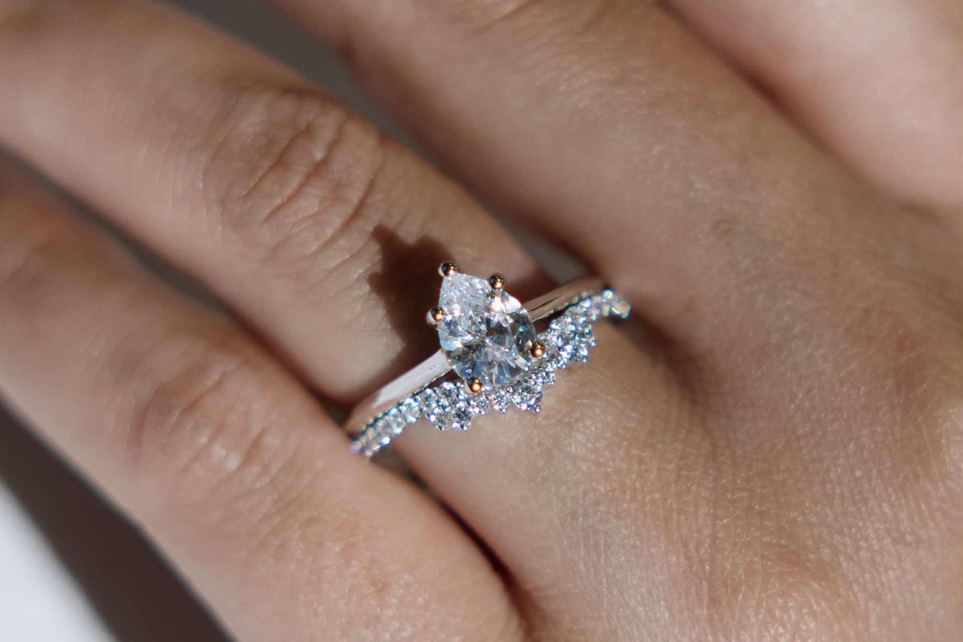 Close-up of a hand wearing a pear-shaped diamond engagement ring with a diamond band.