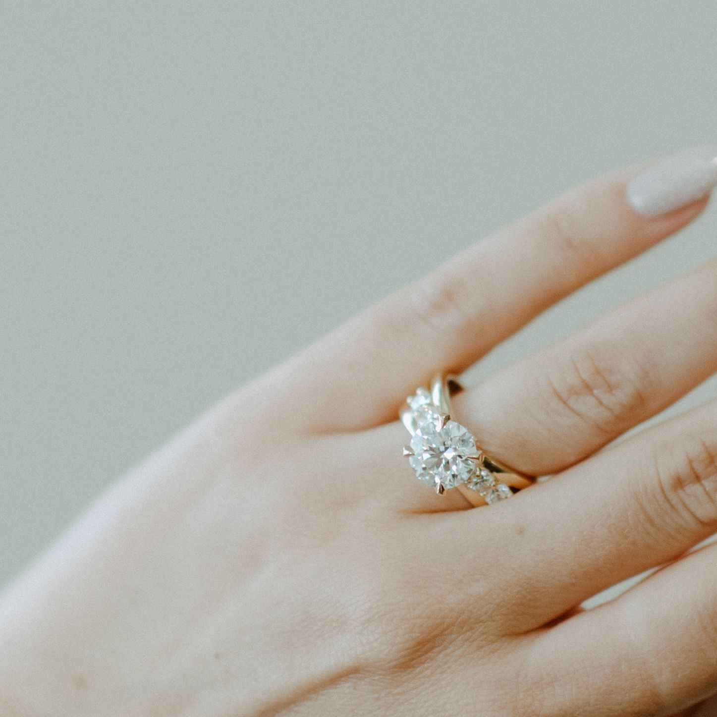 Close-up of a hand wearing a gold ring with three clear stones.