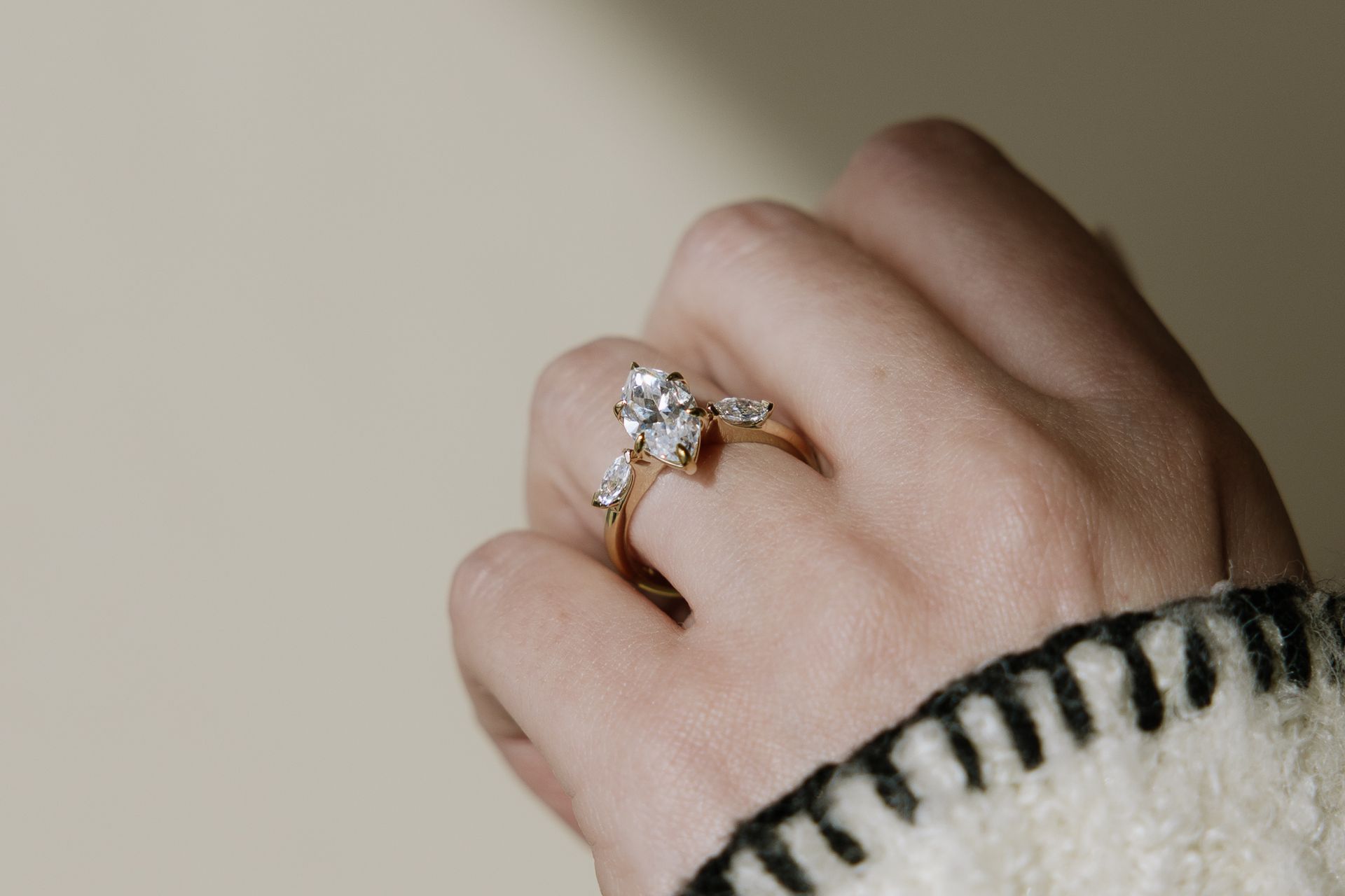 Hand wearing gold ring with oval center stone and two side stones.