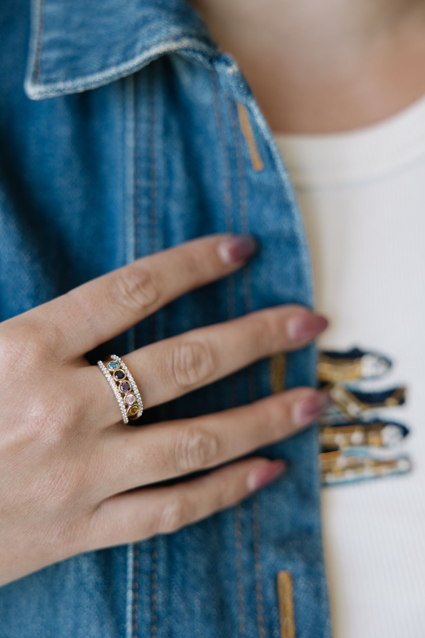 Hand wearing a gold ring with brown and white stones, resting on a denim jacket.