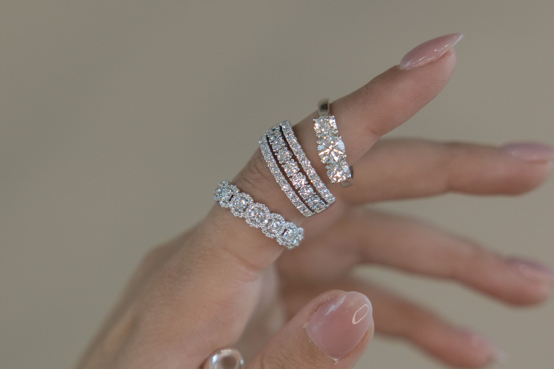 Hand displaying four diamond rings, with clear nail polish.