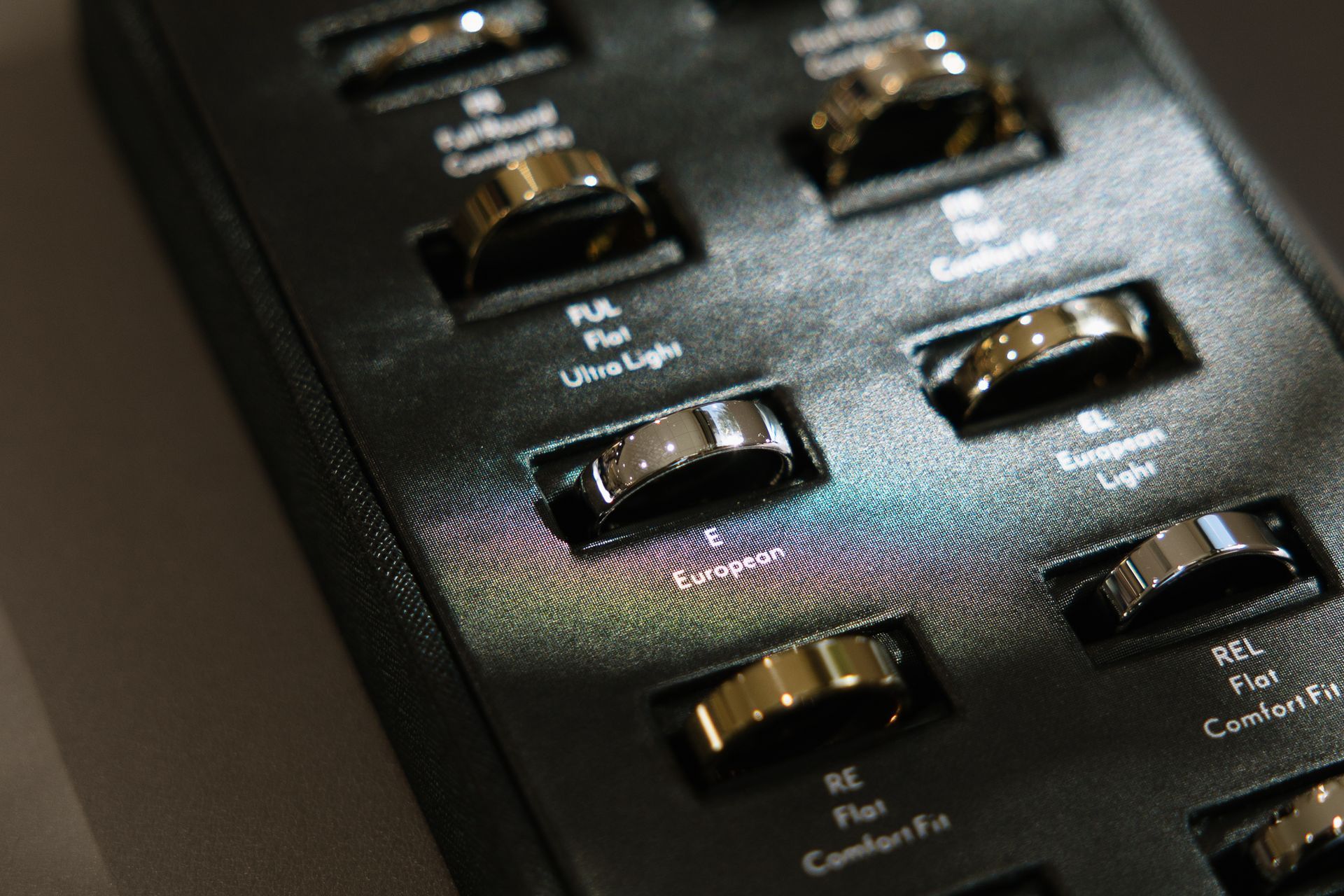 Close-up of a display case with a variety of gold and silver rings, each labeled with a style name.