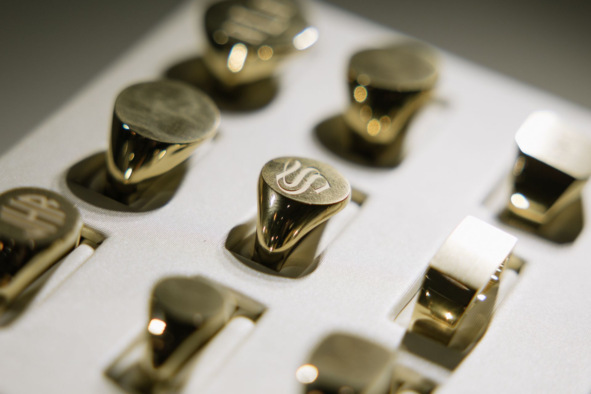 Close-up of a display case holding several gold signet rings, some with engraved initials, reflecting light.