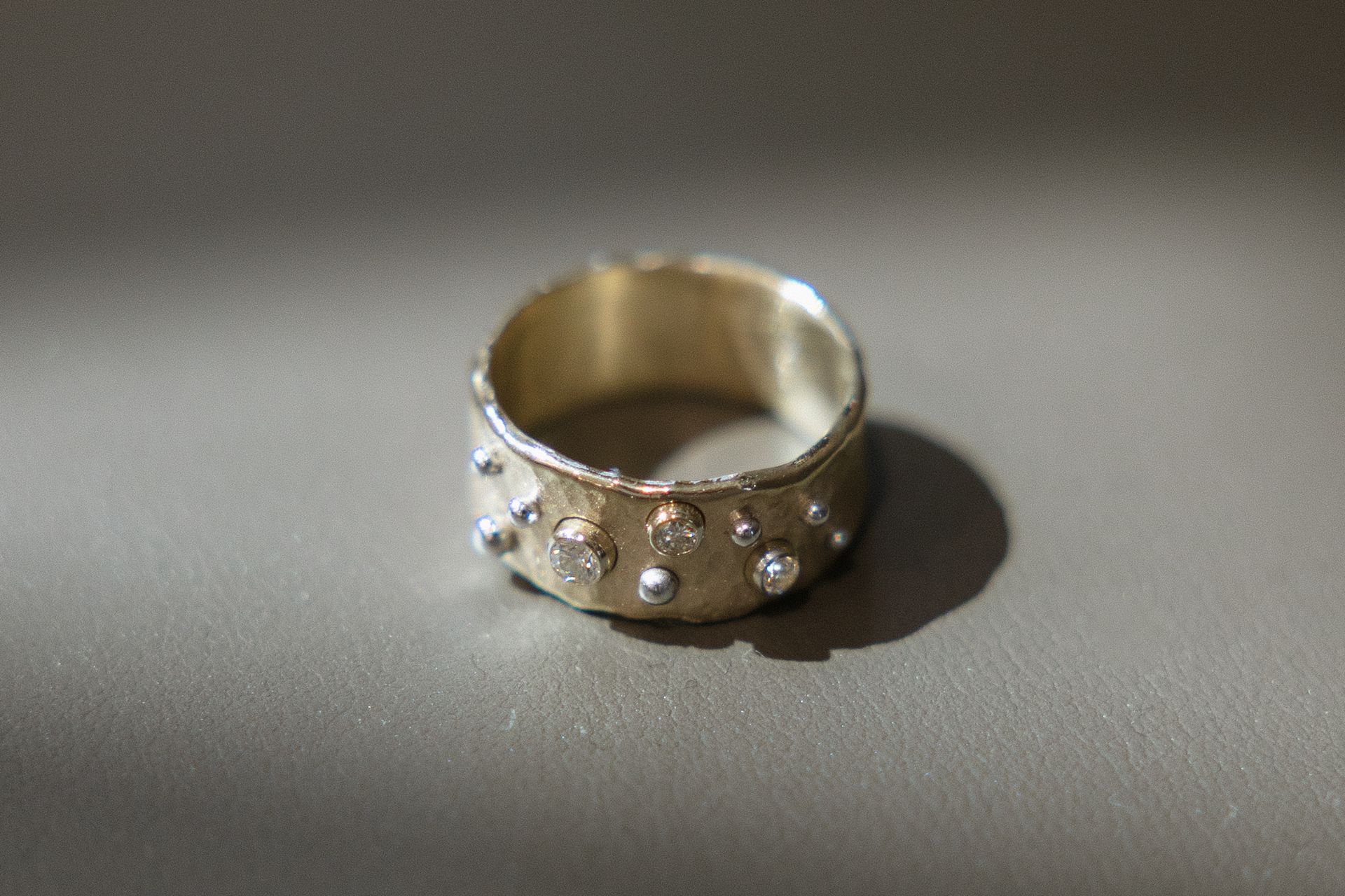 Wide gold ring with textured surface and scattered clear gemstones.