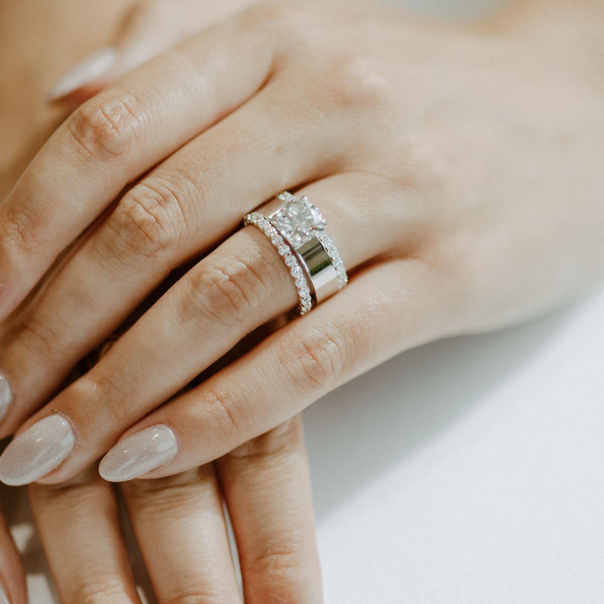 Hand wearing a large diamond ring and a matching band. Light nail polish.