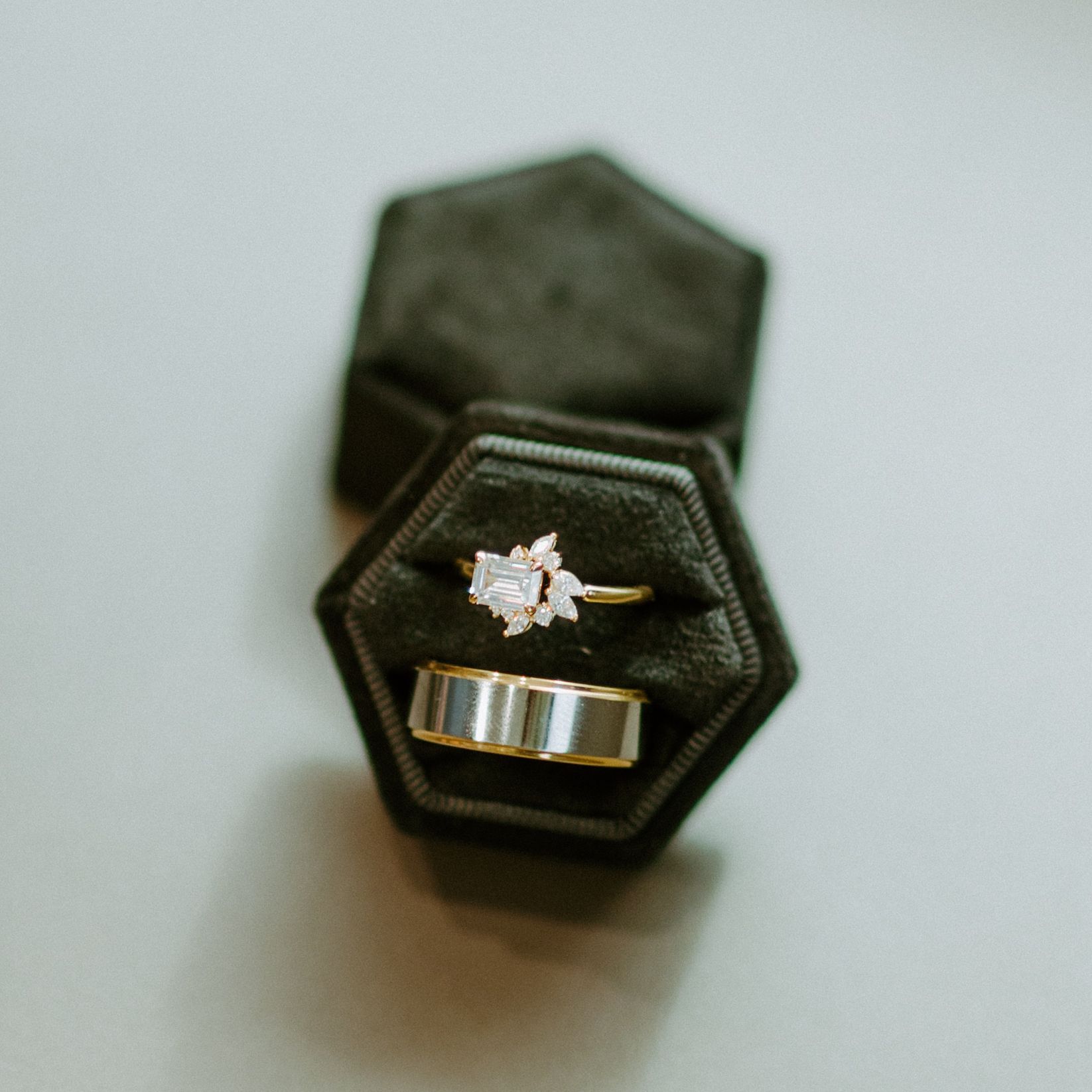 Two rings in a dark green velvet hexagonal box; engagement ring with a cluster of stones, simple gold band.