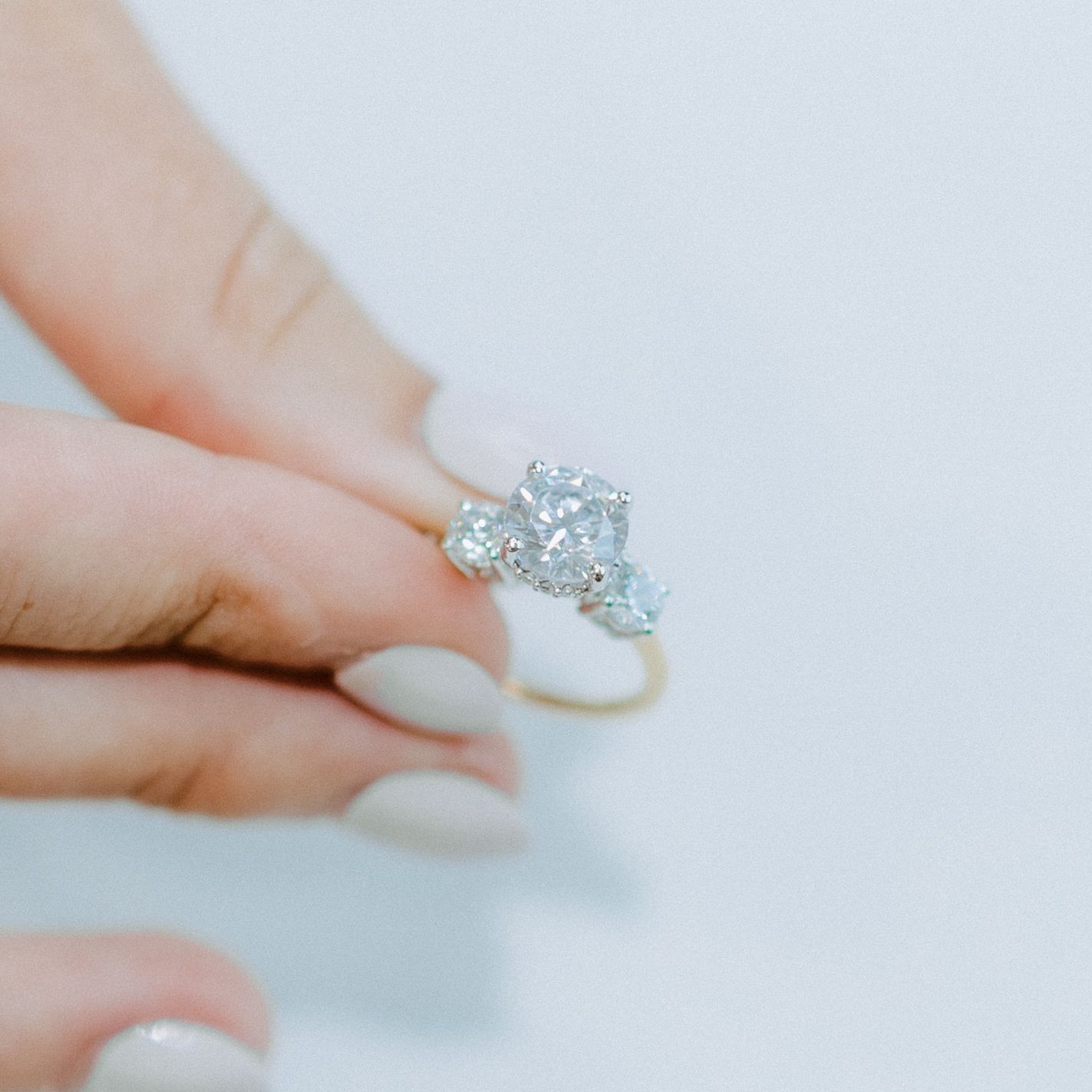 Hand holding a gold ring with a large oval diamond and two smaller diamonds.