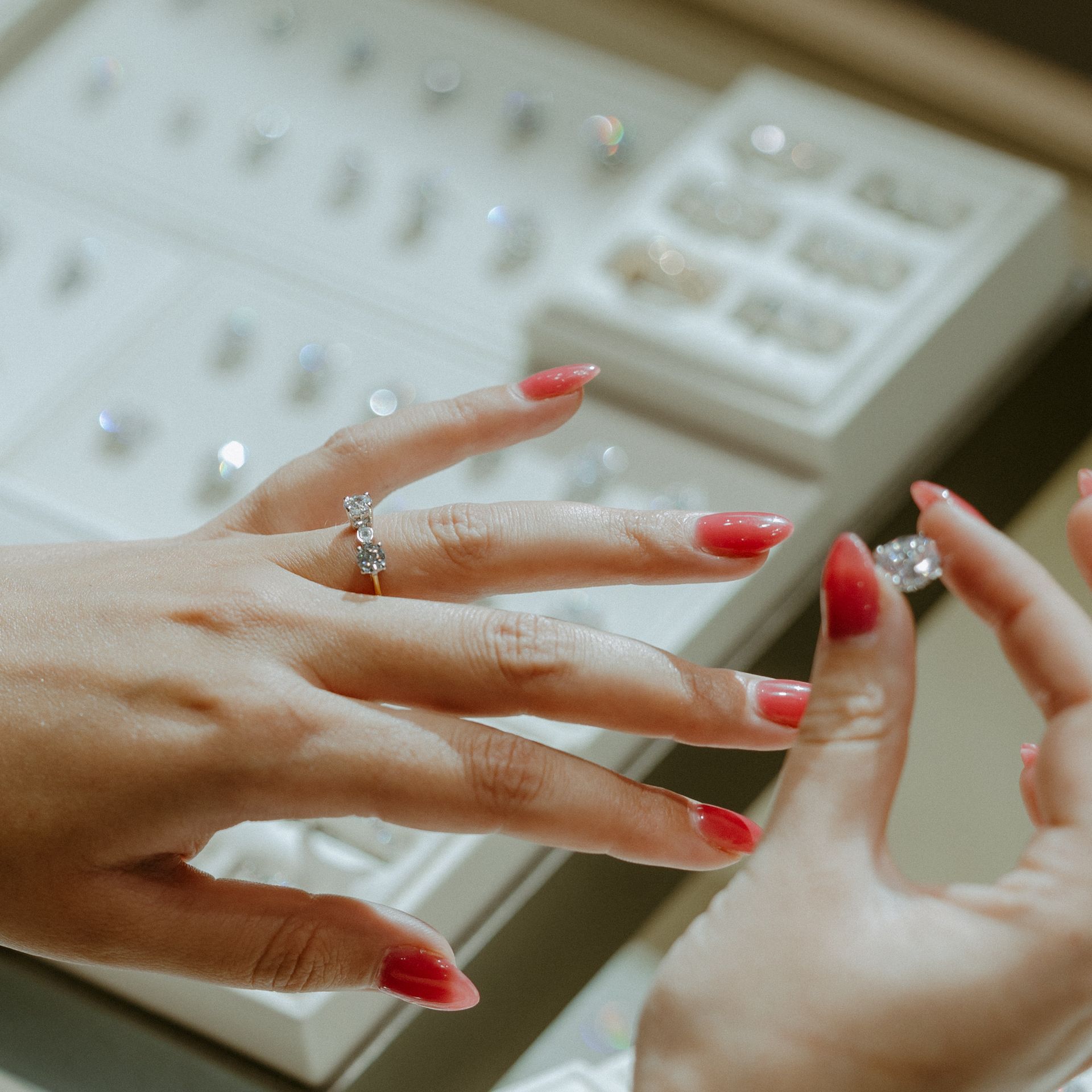 Hands examining rings in a jewelry store display case, red nails.