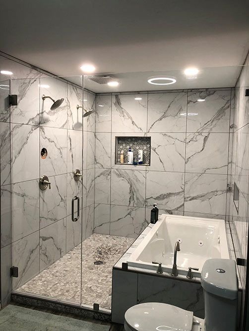 A bathroom with marble tiles , a tub , a toilet , and a walk in shower.