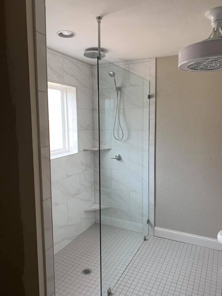 A bathroom with a walk in shower with a glass door and a window.