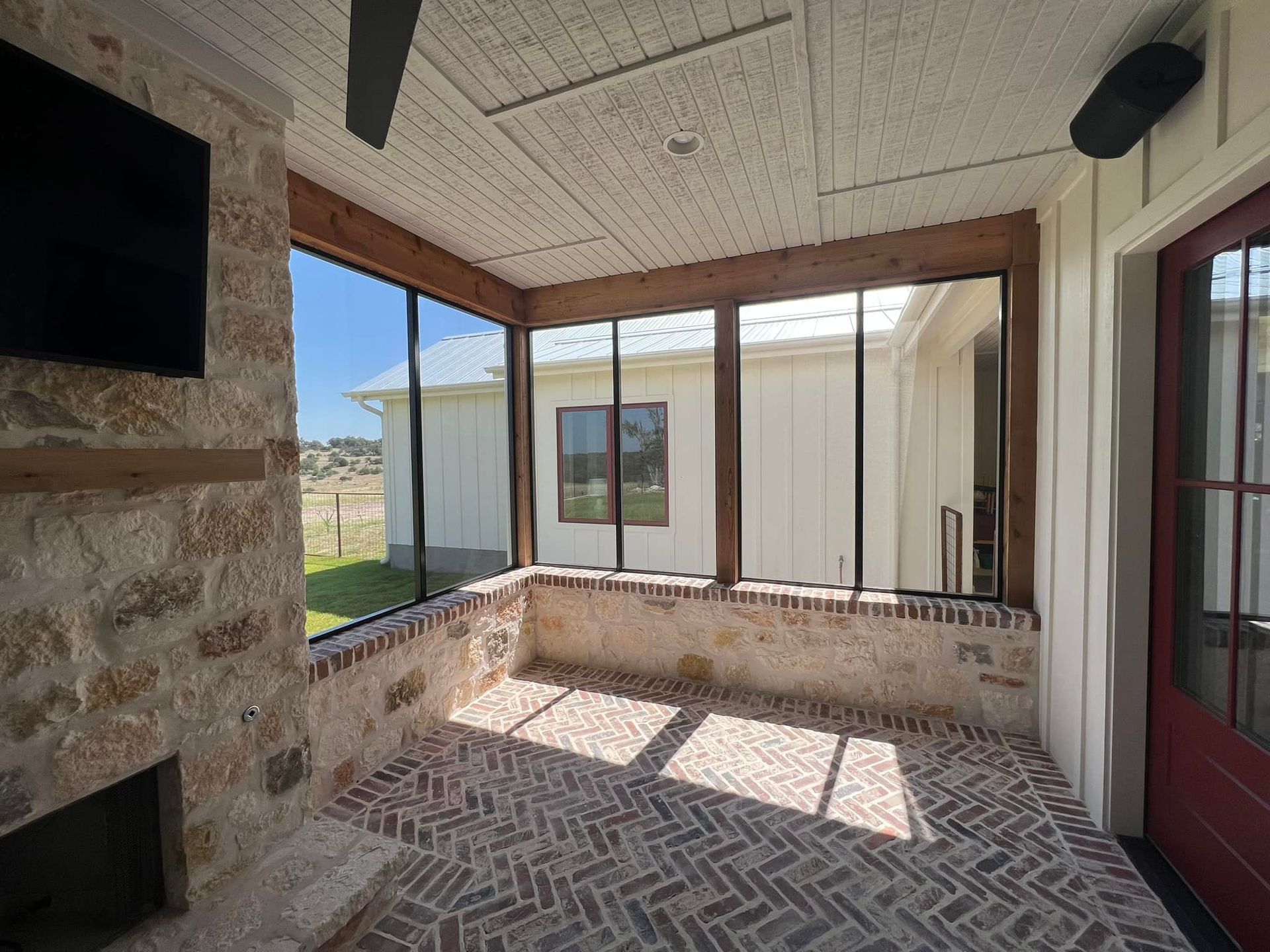 A screened in porch with a fireplace and a flat screen tv.
