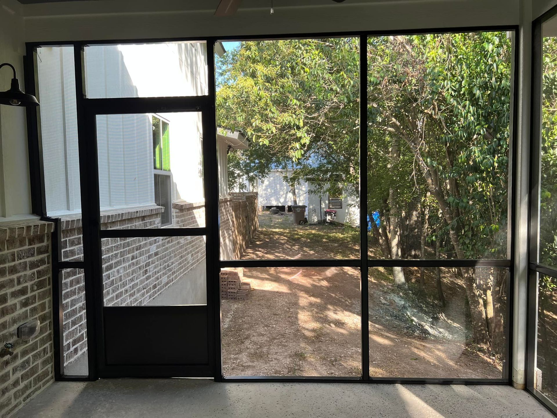 A screened in porch with a brick wall and trees in the background.