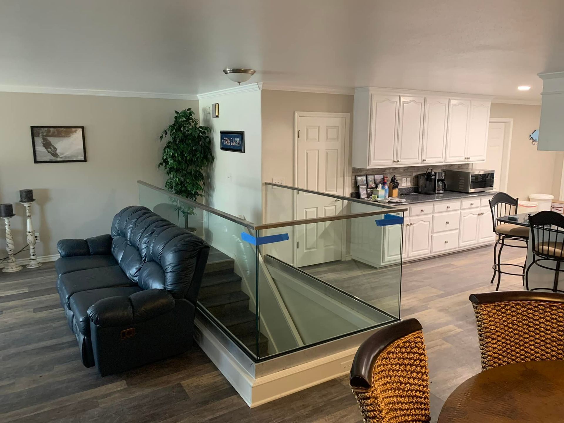 A living room with a black couch and a glass railing leading to a kitchen.