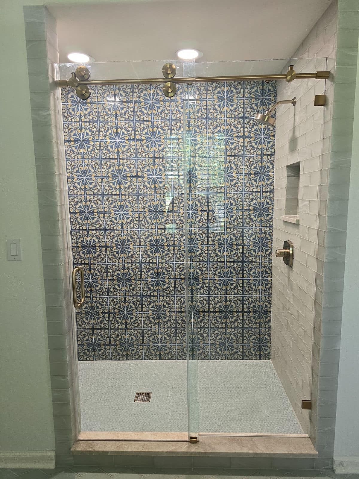 A shower with a glass door and a blue and white tile wall.