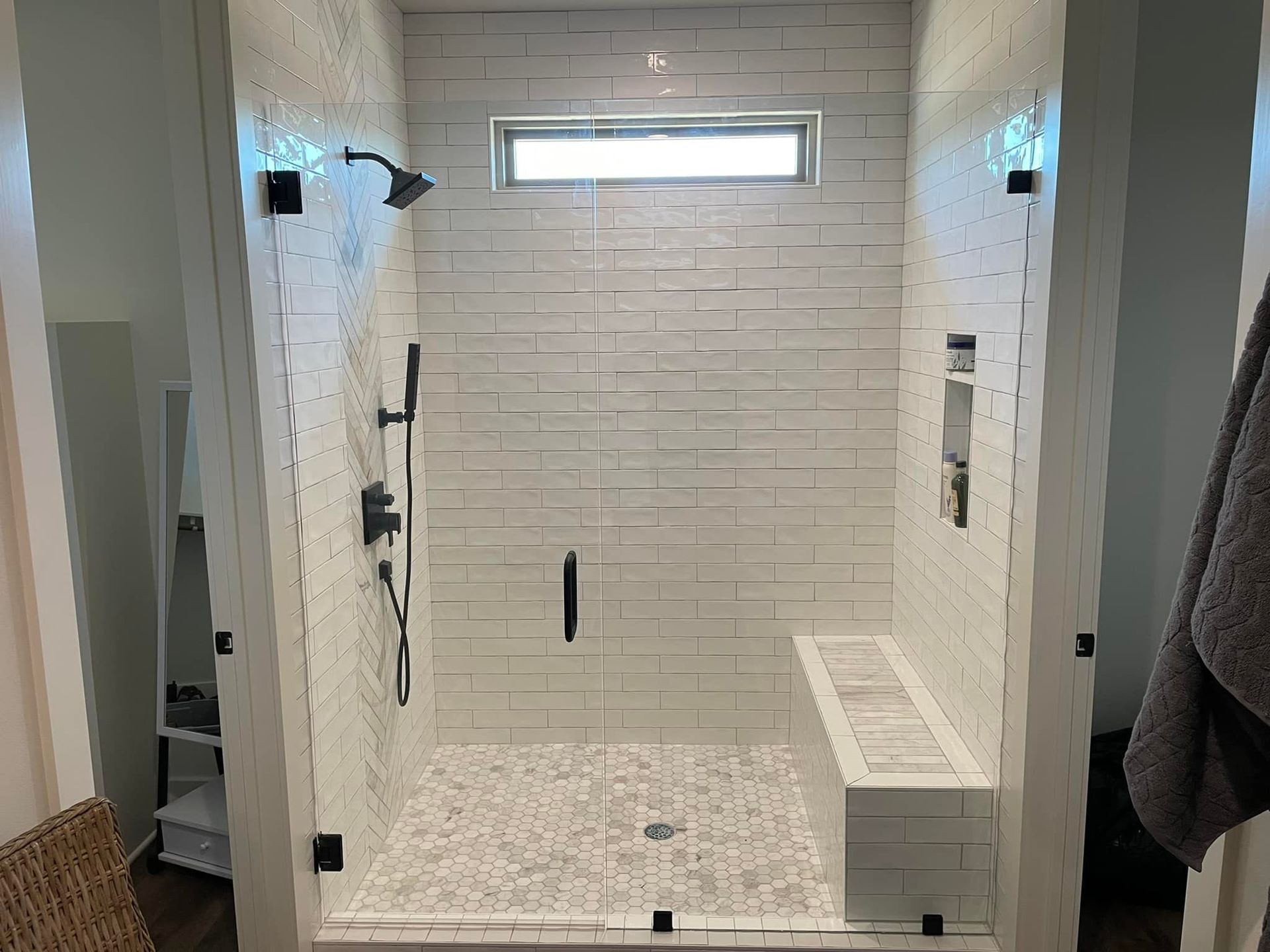 A bathroom with a walk in shower with a bench and a window.