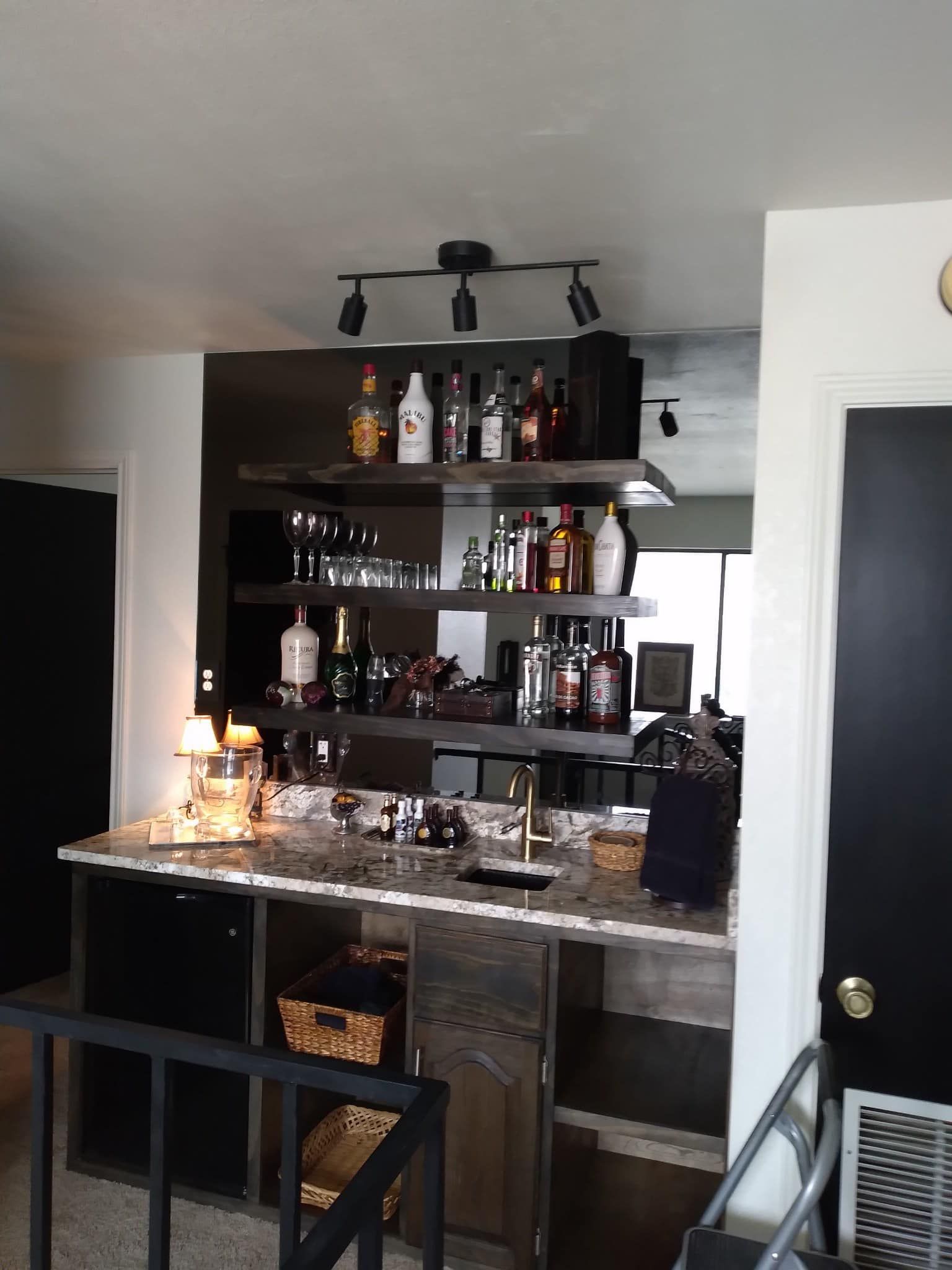 A kitchen with a bar and lots of bottles on shelves
