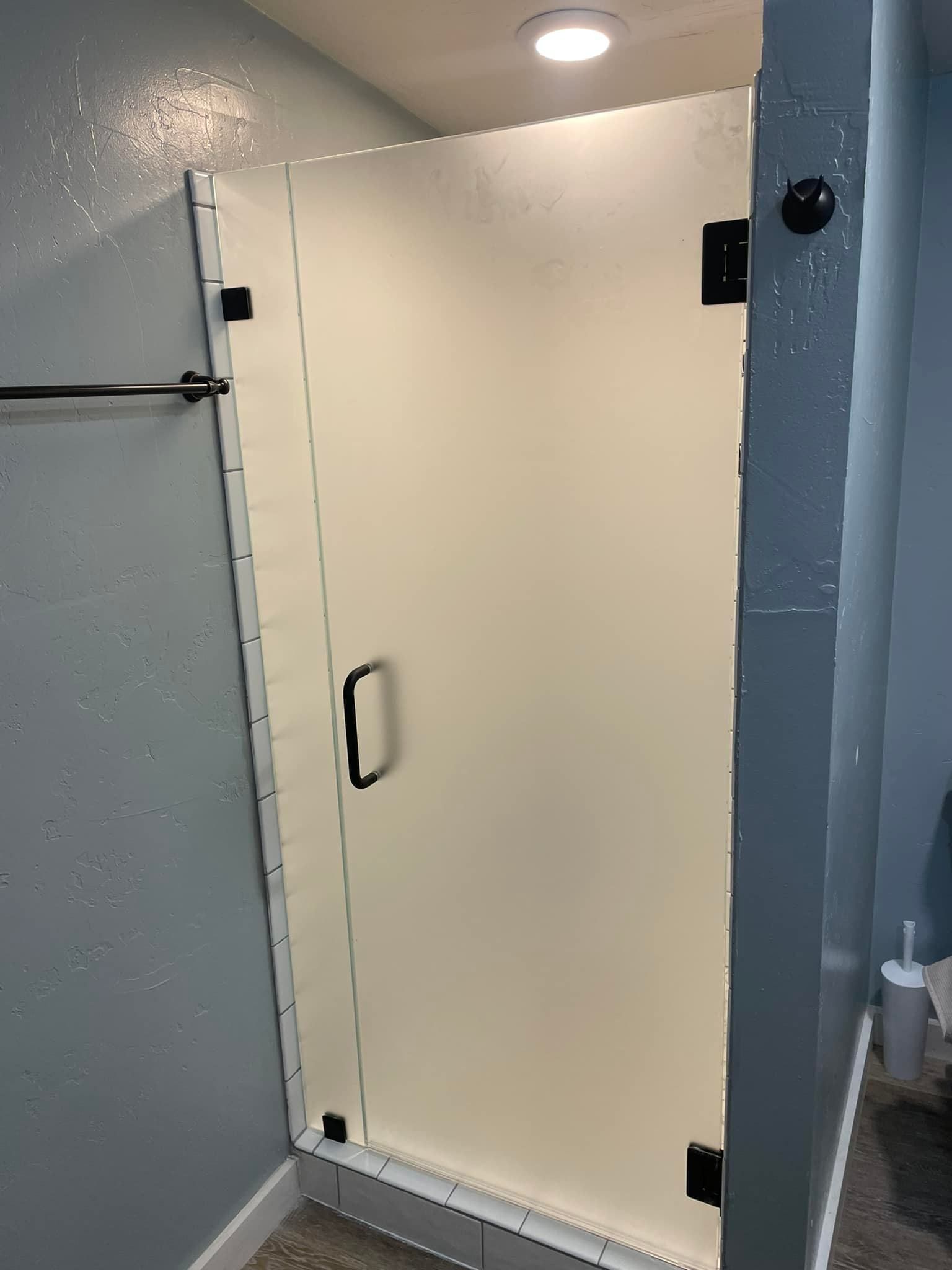 A white shower door with a black handle in a bathroom.