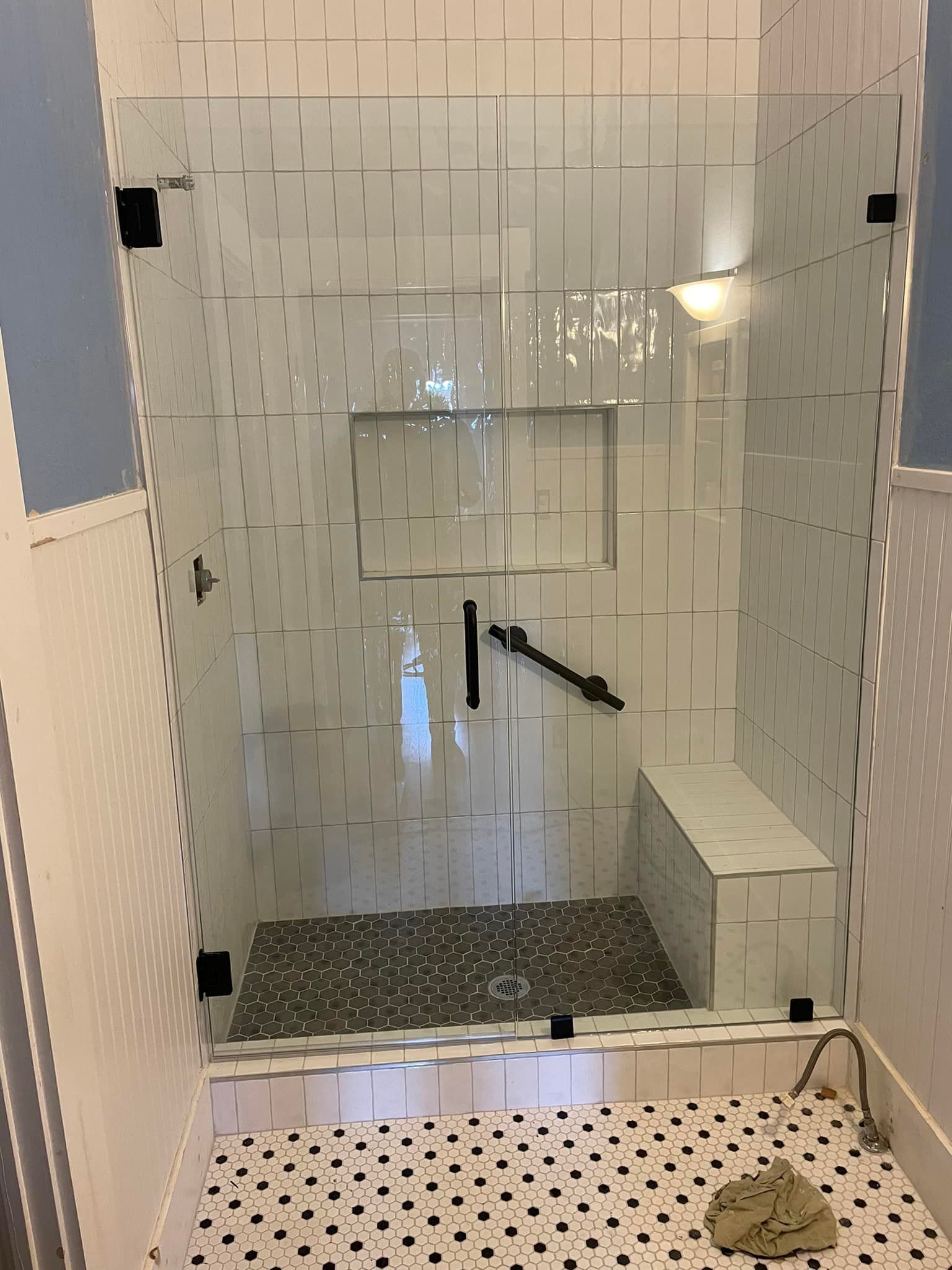 A bathroom with a walk in shower with a glass door and a bench.