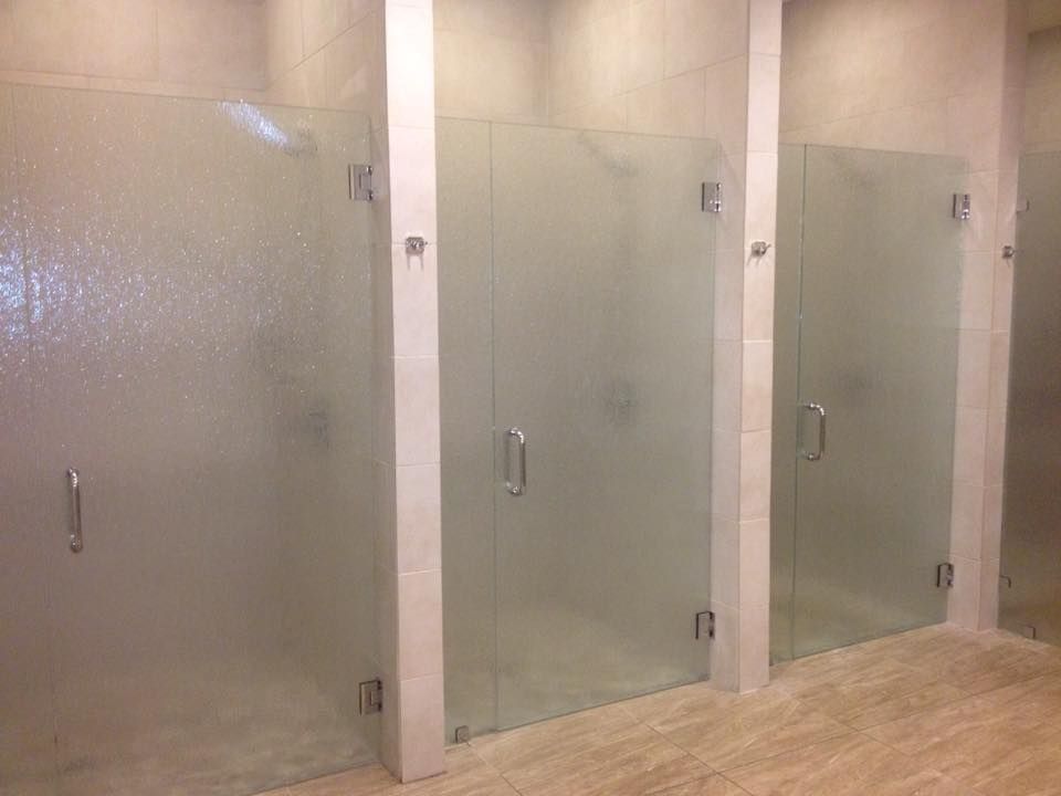 A row of shower stalls with frosted glass doors in a bathroom.