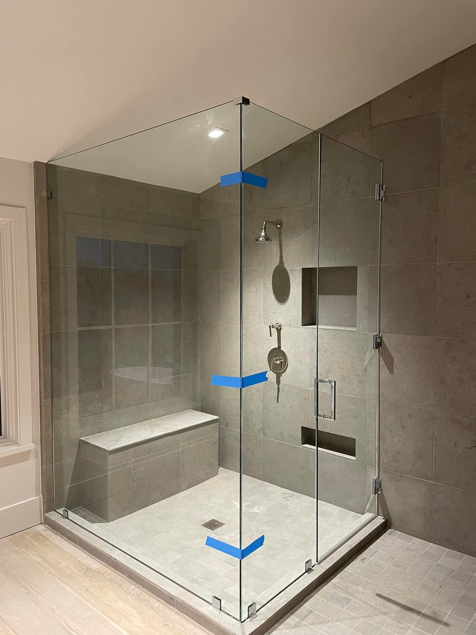 A bathroom with a walk in shower with a glass door and a bench.