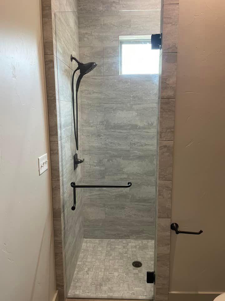 A bathroom with a walk in shower with a glass door and a window.