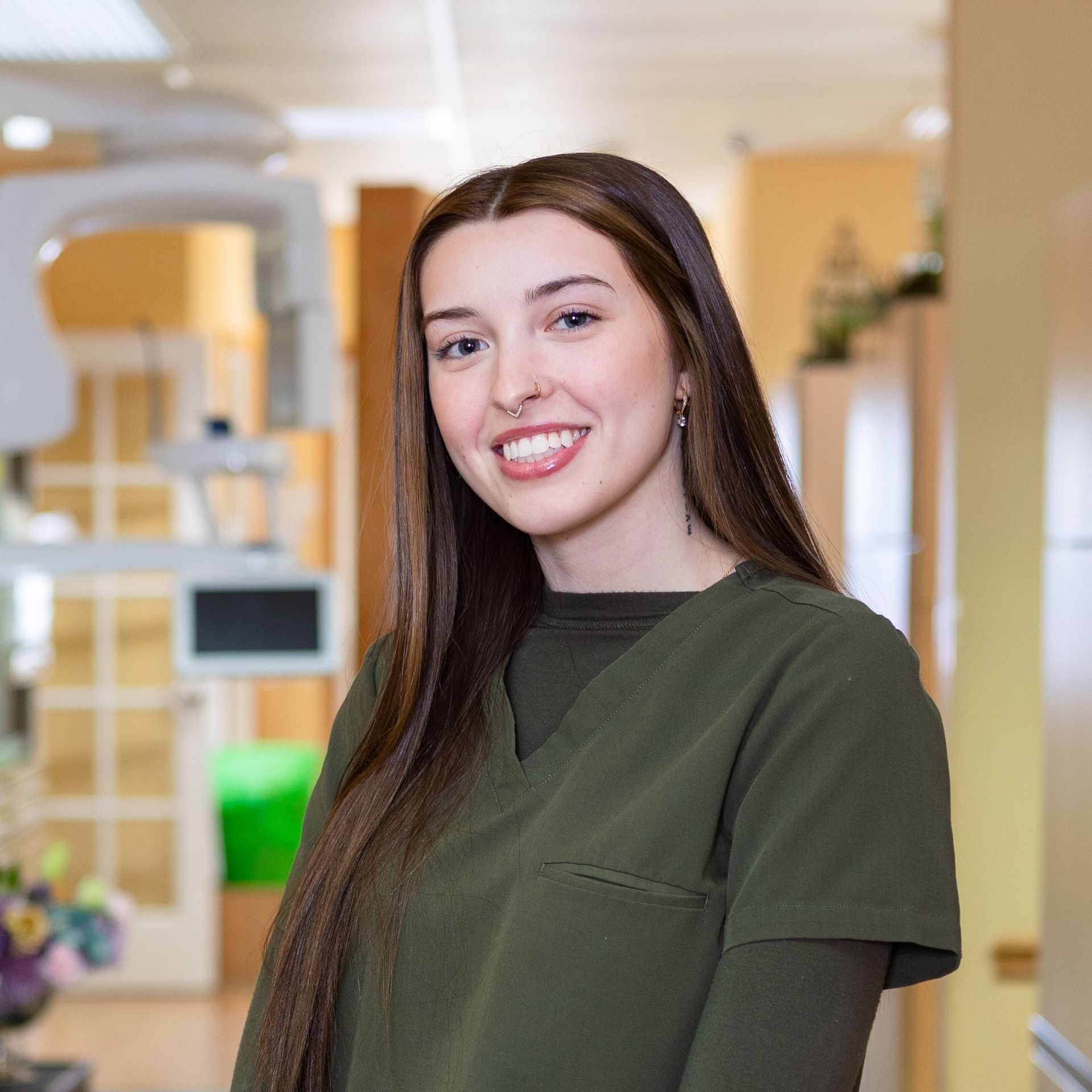 A woman in a green scrub top is smiling in a dental office.